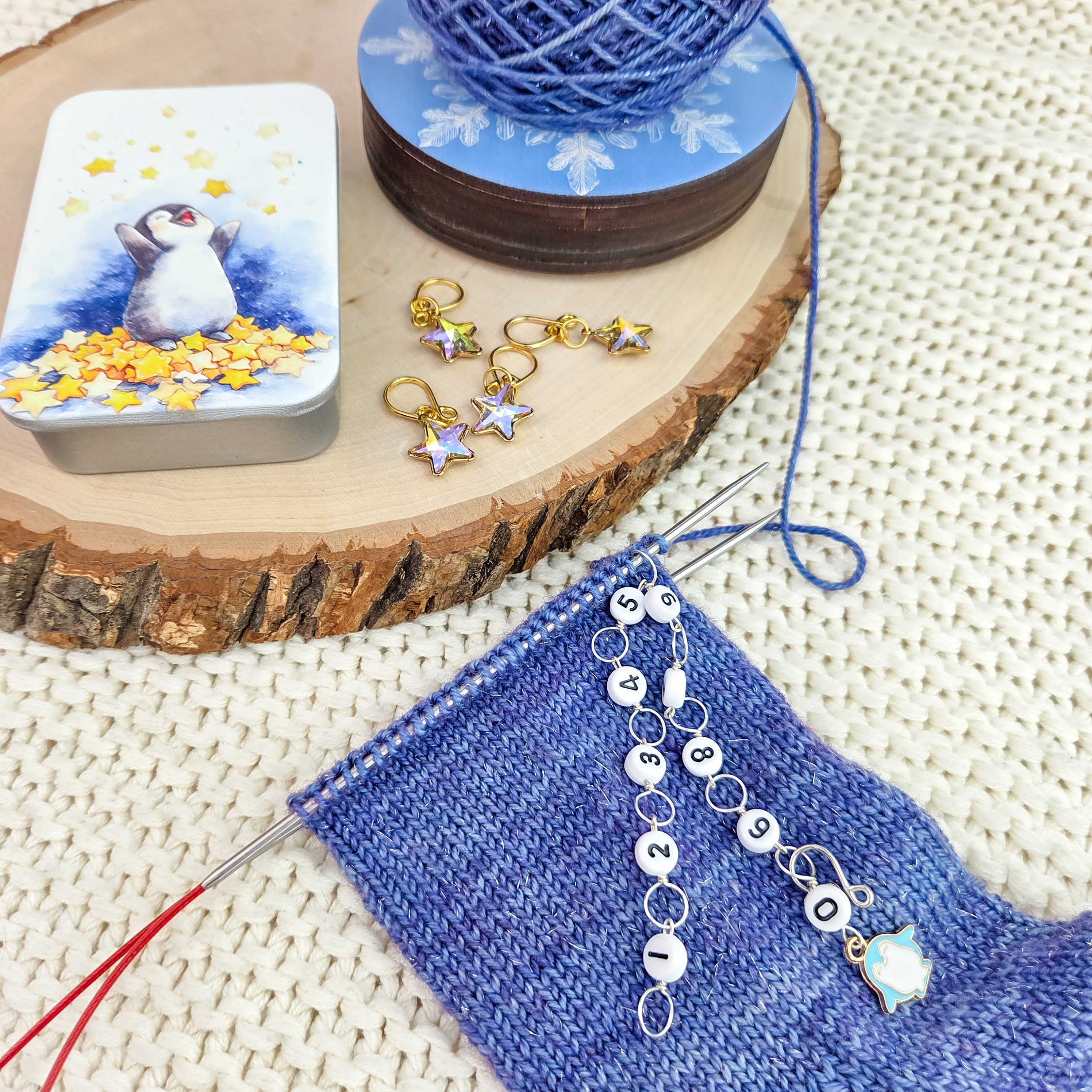 Close-up of blue knit swatch in progress with the Original Chain Row Counter attached to bamboo needles showing chain links numbered for row tracking