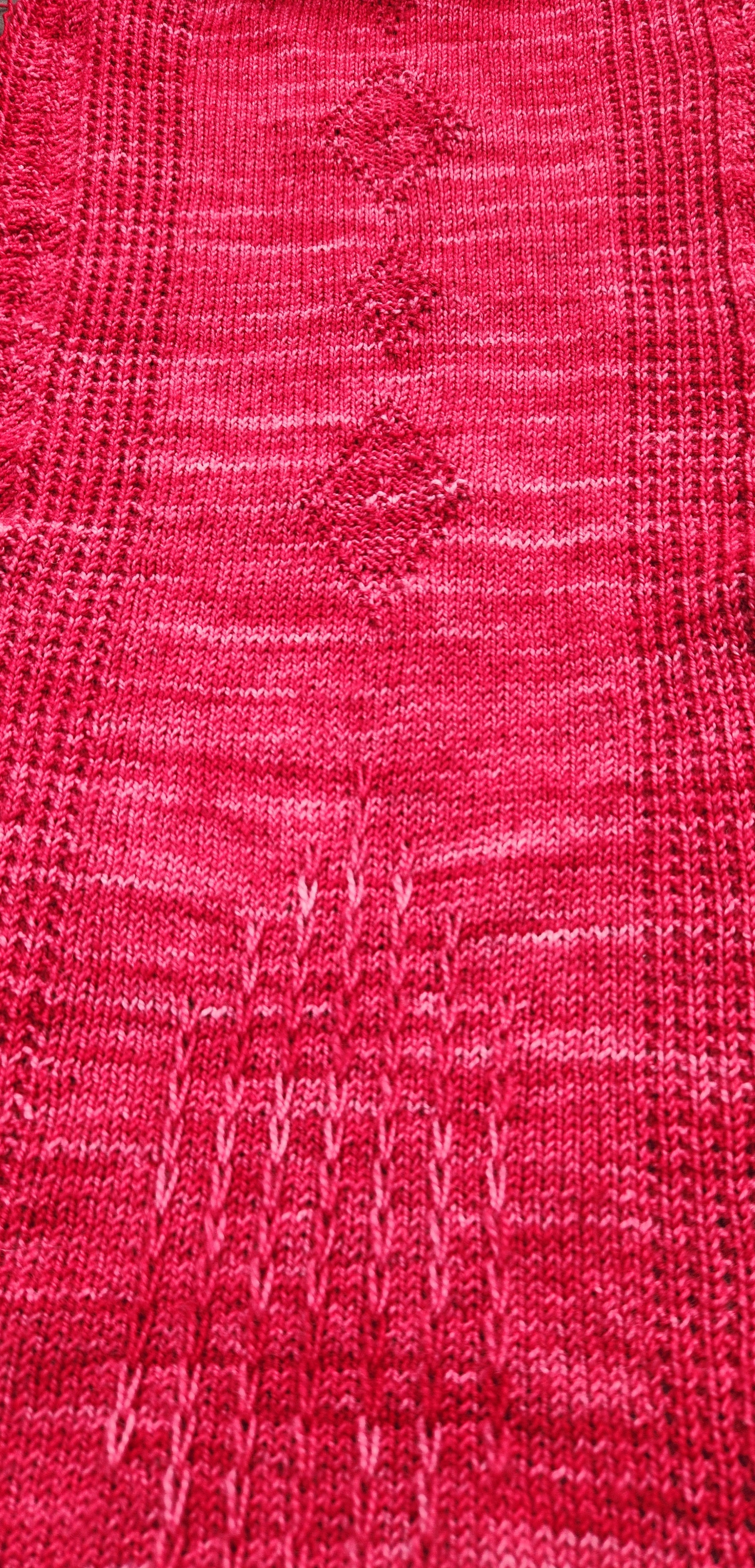 Close-up of the Revenge in Lido Wrap knitted fabric showing the openwork lace stitch pattern in coral pink fingering weight yarn