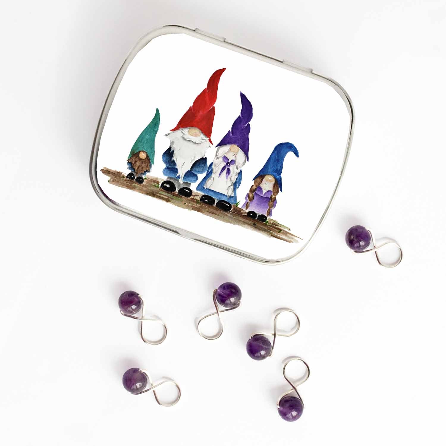 Small hinged Gnome Family tin with watercolor gnome family lid, shown beside six purple beaded stitch markers