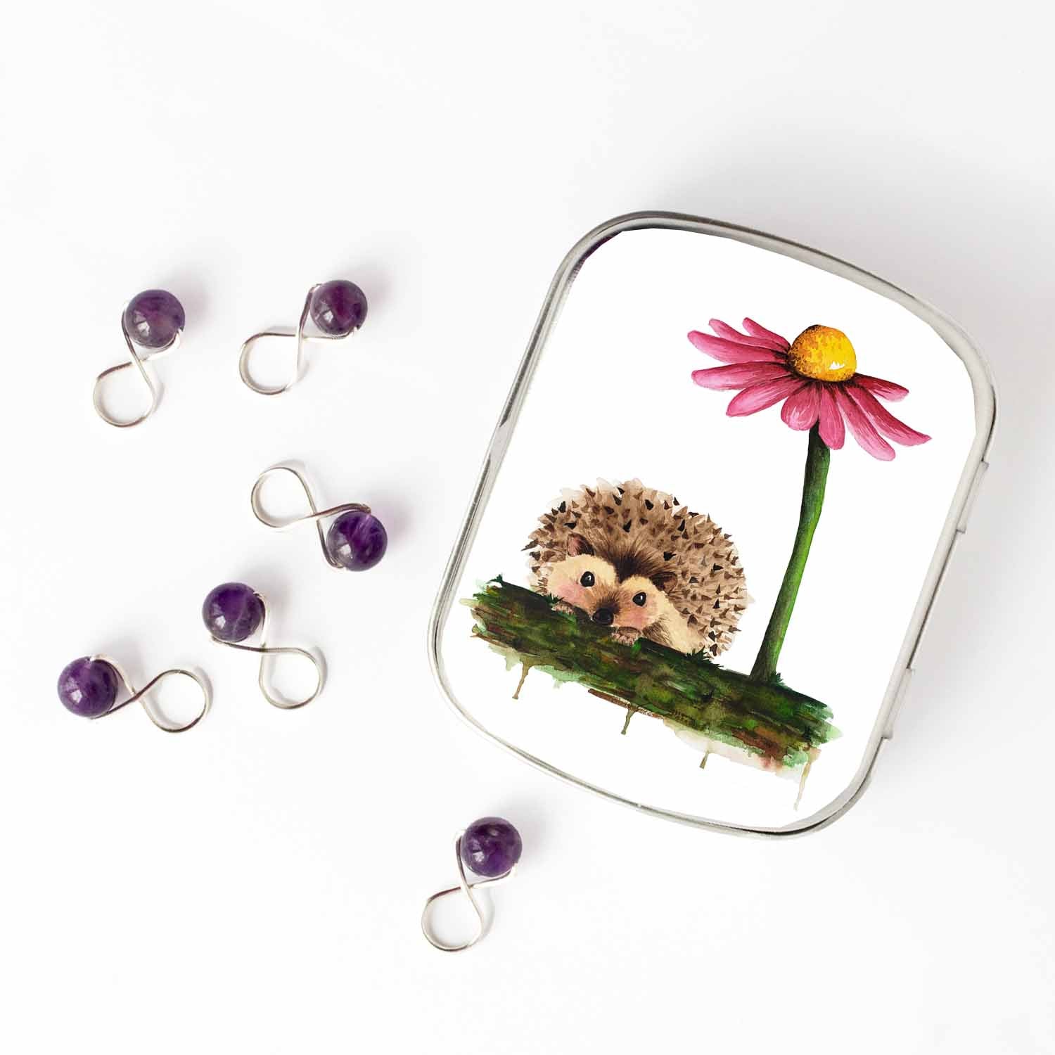 Small hinged Hedgehog tin with watercolor hedgehog lid, shown beside six purple beaded stitch markers