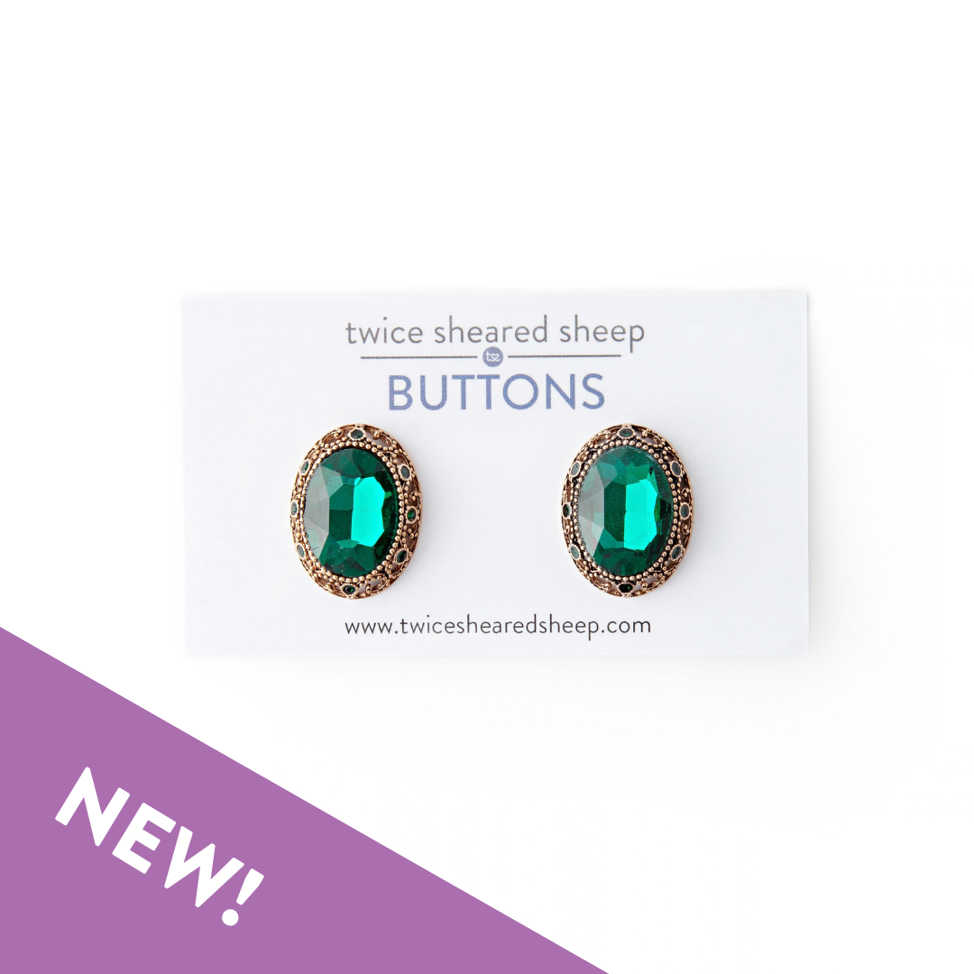 Two oval emerald green jewel buttons with antique gold filigree settings on a Twice Sheared Sheep buttons card, with a purple NEW banner