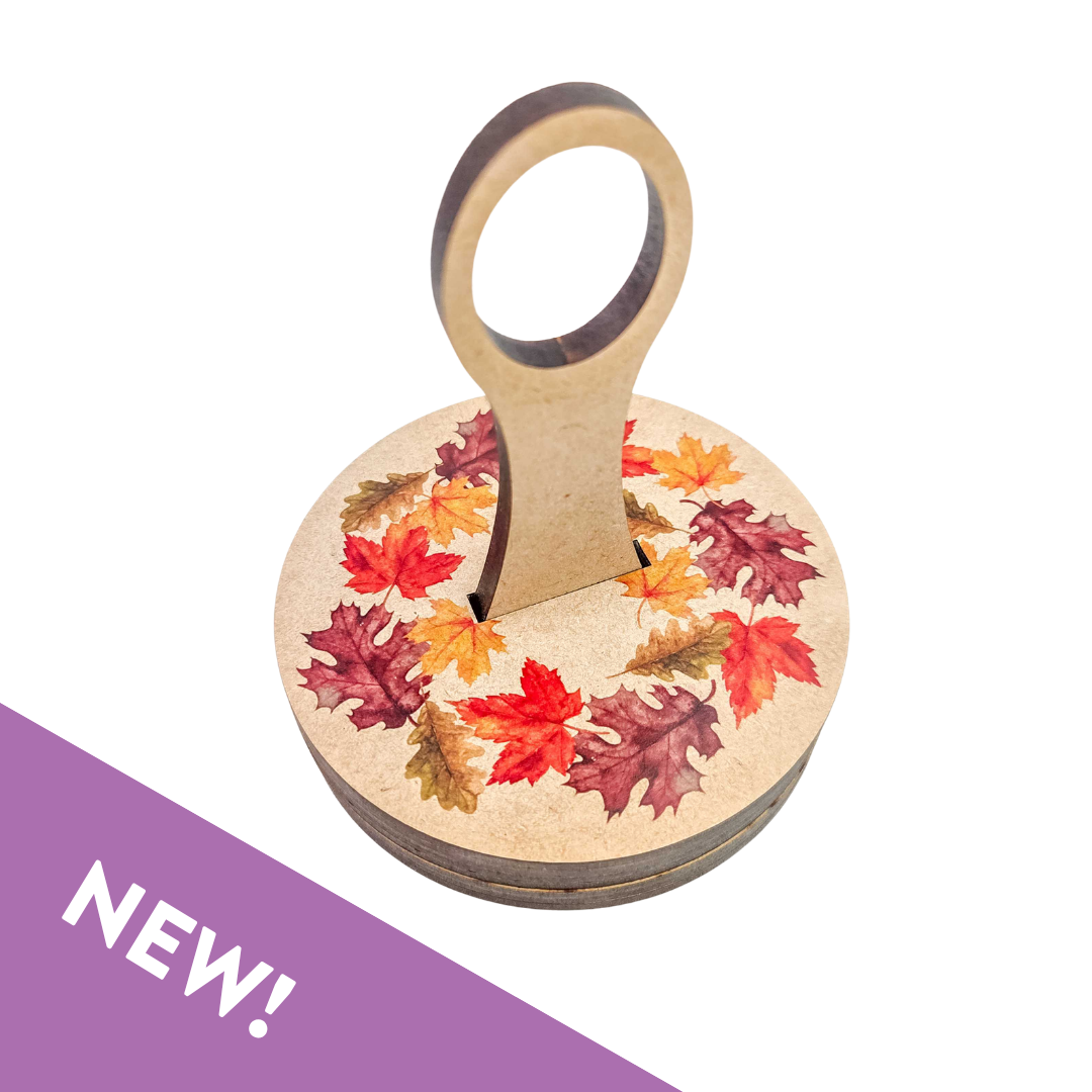 Fall Leaves Carousel, a round wooden yarn holder printed with a wreath of red, orange and gold fall leaves and an upright yarn guide, with a purple NEW banner