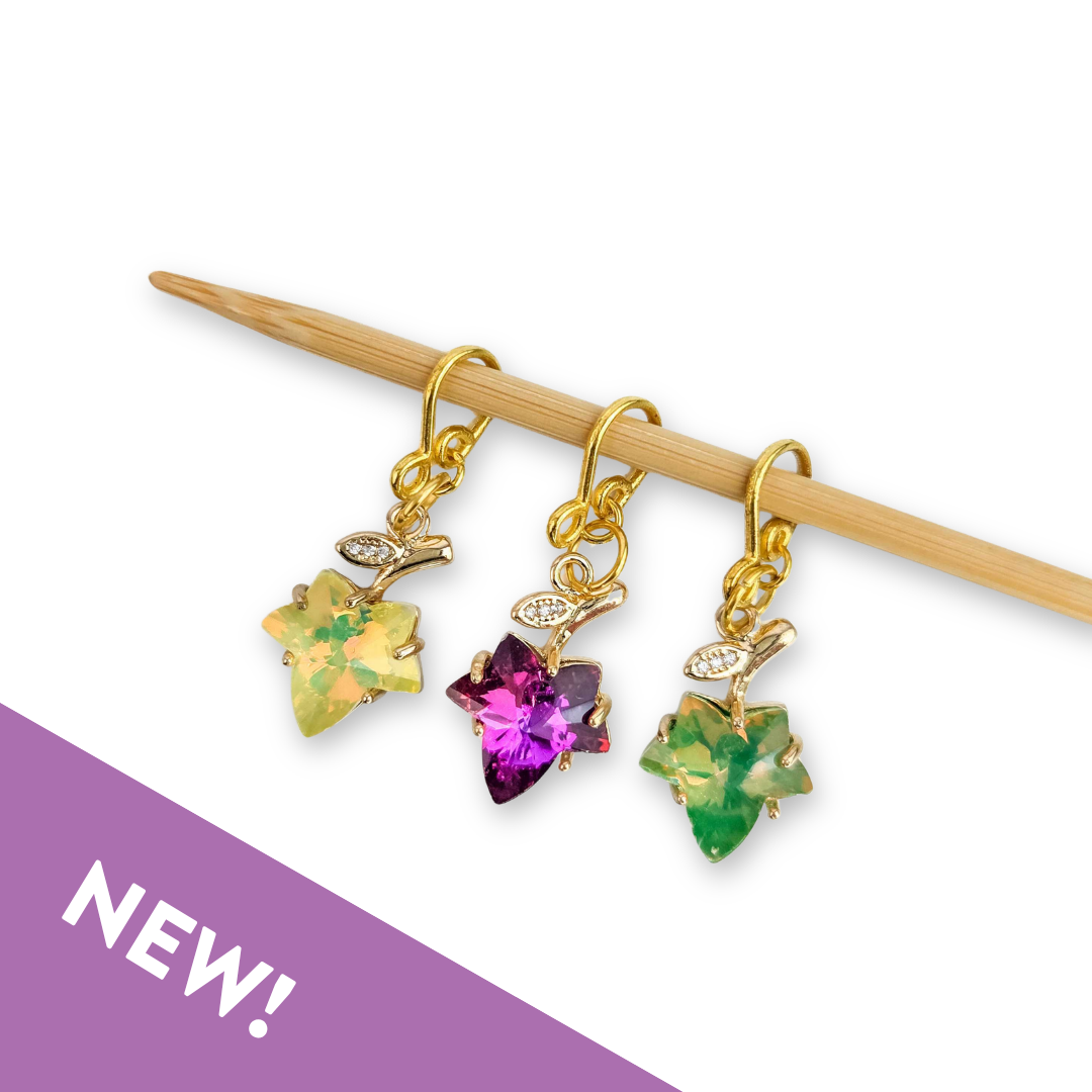 Three gold Fall Leaves Melody stitch markers set with yellow, magenta and green crystal leaves hanging from a bamboo knitting needle, with a purple NEW banner