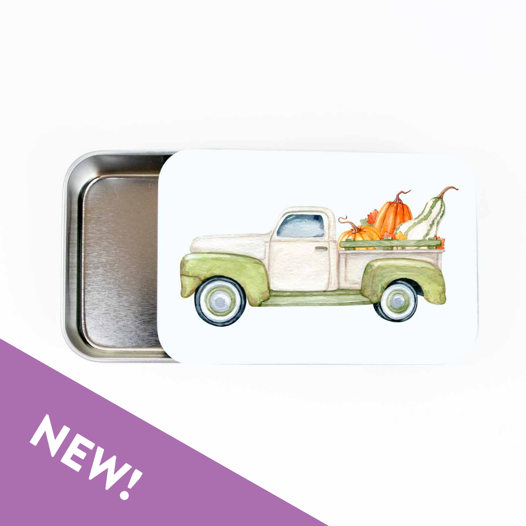 Slide top stitch marker storage tin with a watercolor green pickup truck carrying pumpkins and gourds, with a purple NEW banner