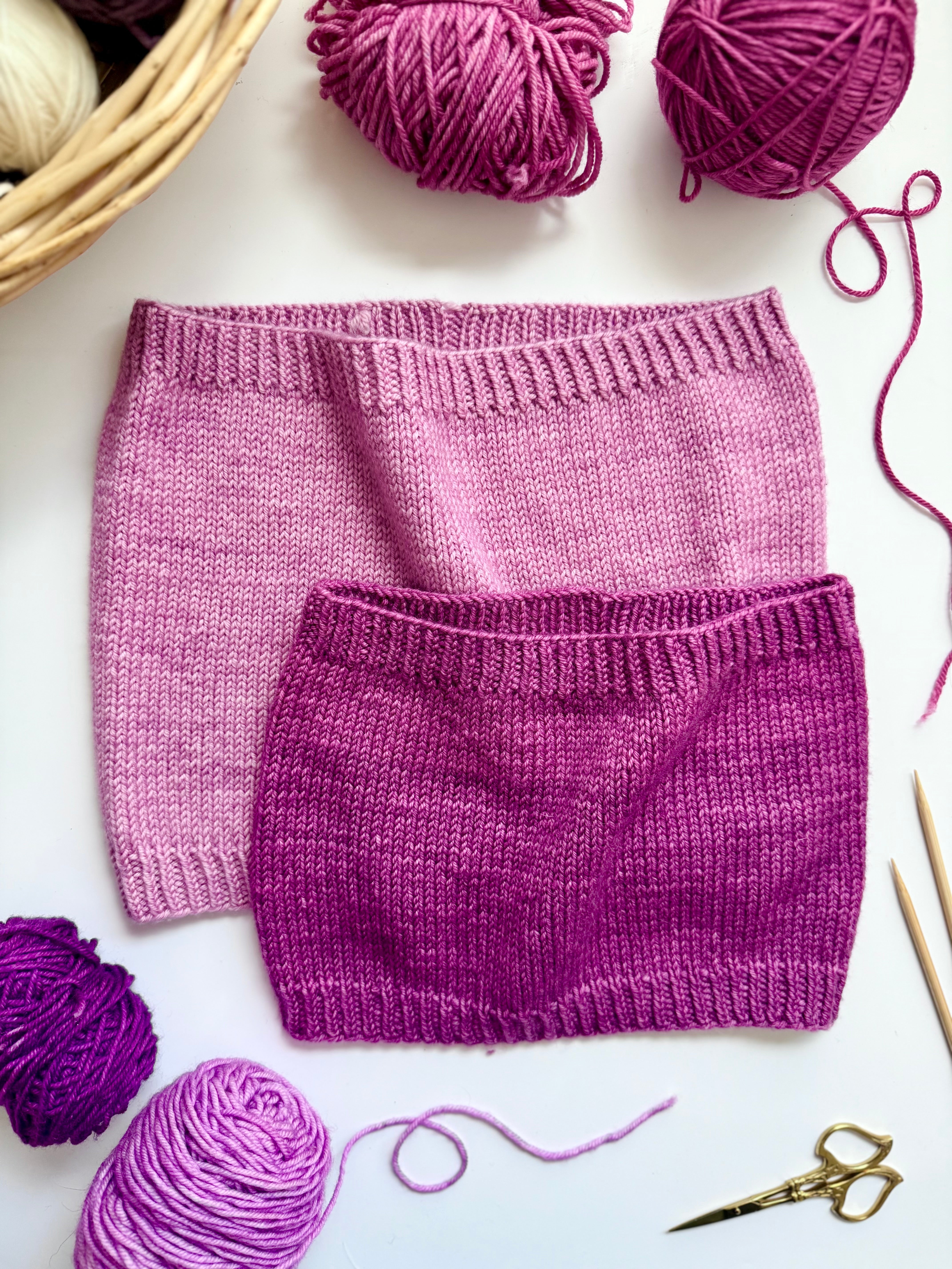 Two Base Doodle Standard Cowls in pink and magenta with yarn and scissors