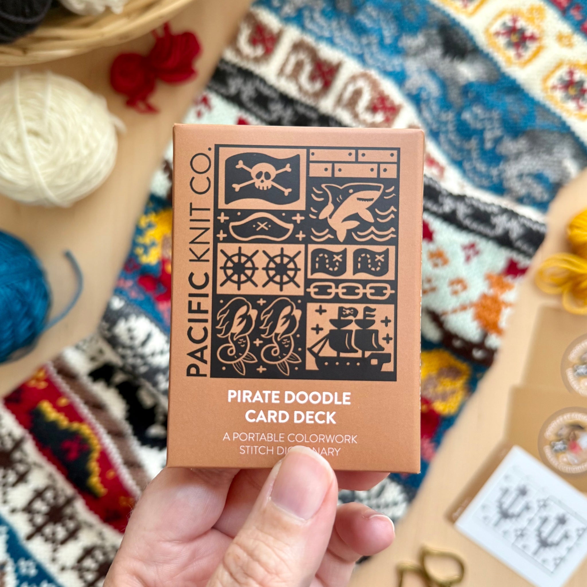 Hand holding the tan Pirate Doodle Card Deck by Pacific Knit Co tuckbox