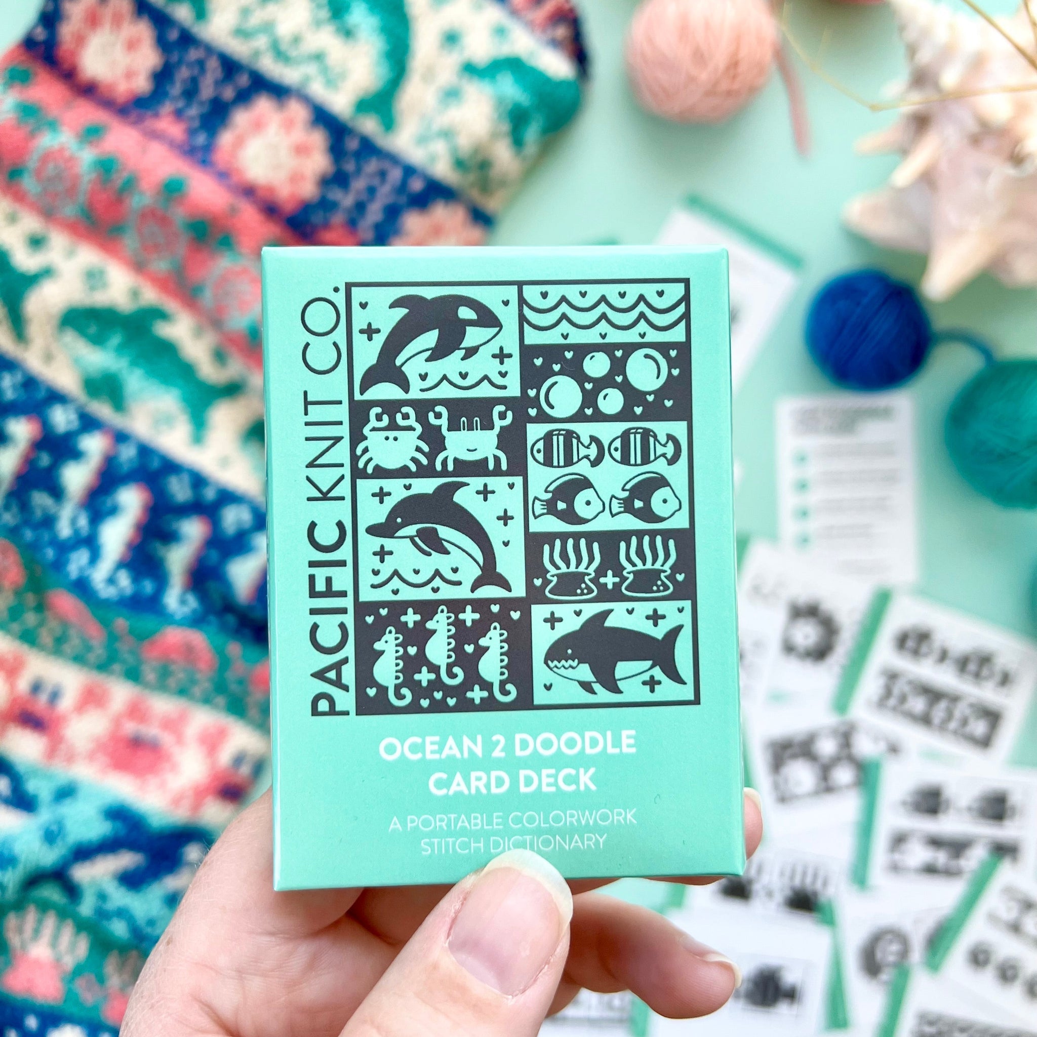 Hand holding the mint green Ocean 2 Doodle Card Deck by Pacific Knit Co tuckbox