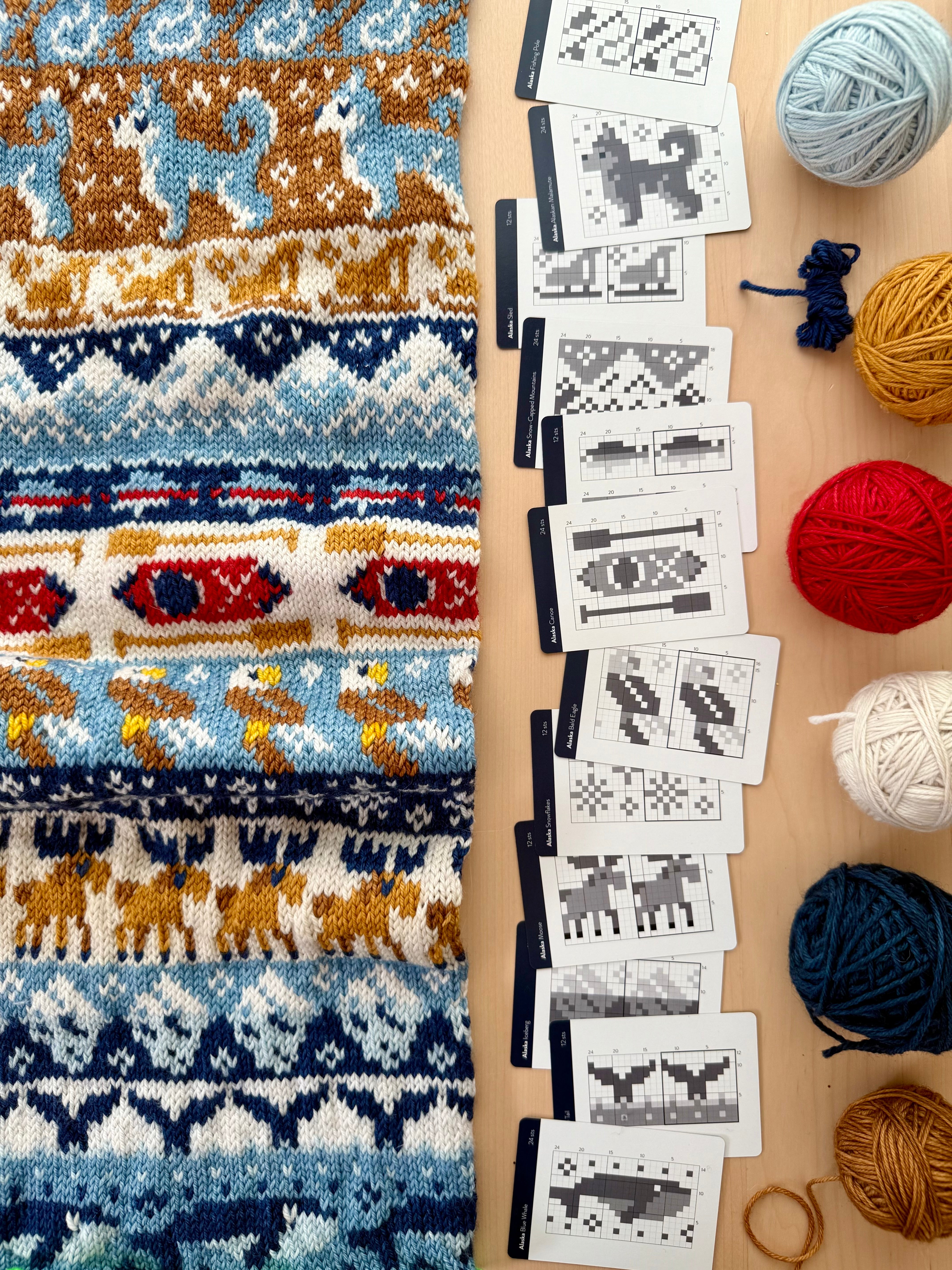 Alaska Doodle chart cards beside a blue and gold colorwork knit and yarn balls