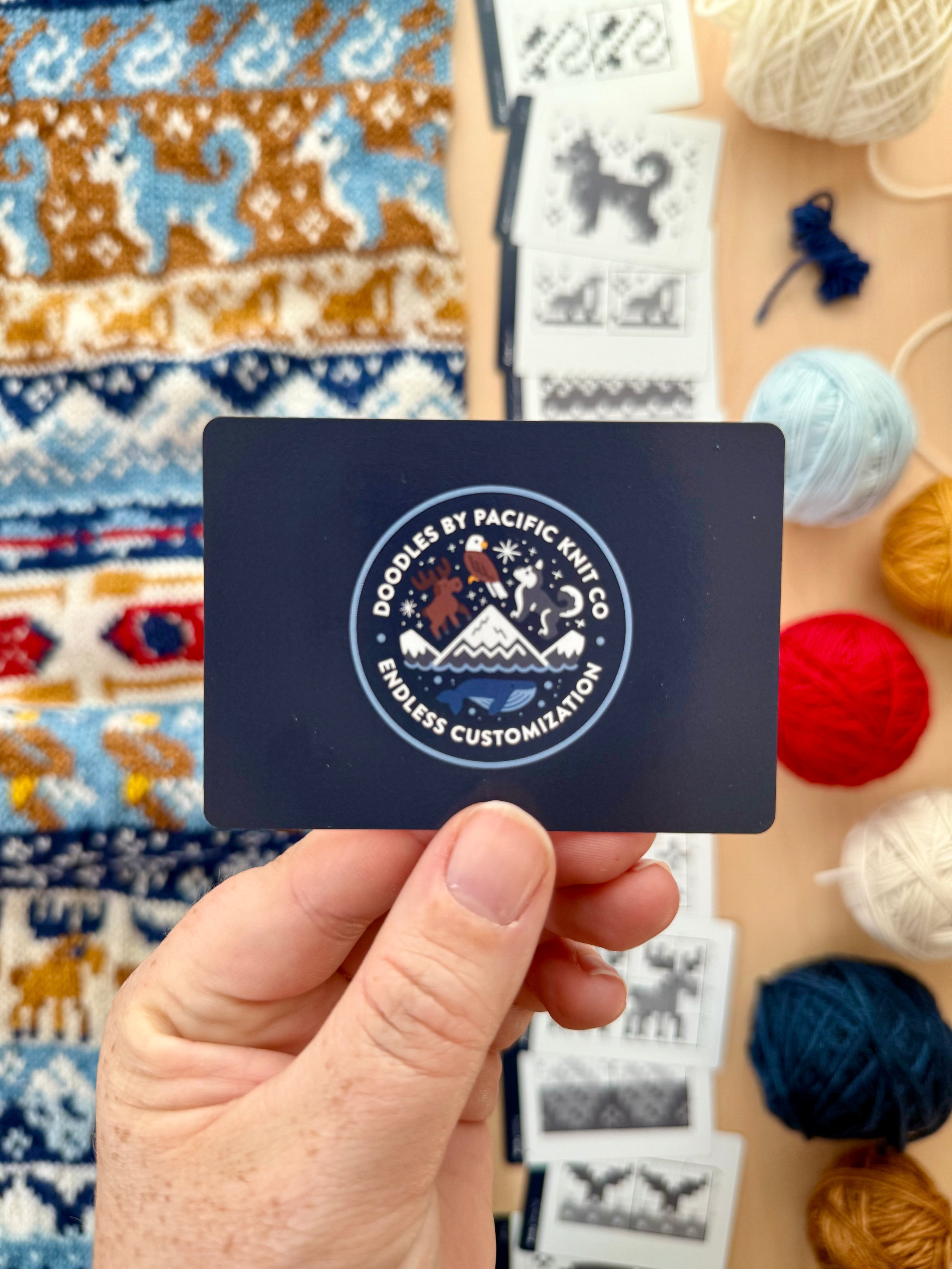 Hand holding the navy Pacific Knit Co card back with the Doodles logo