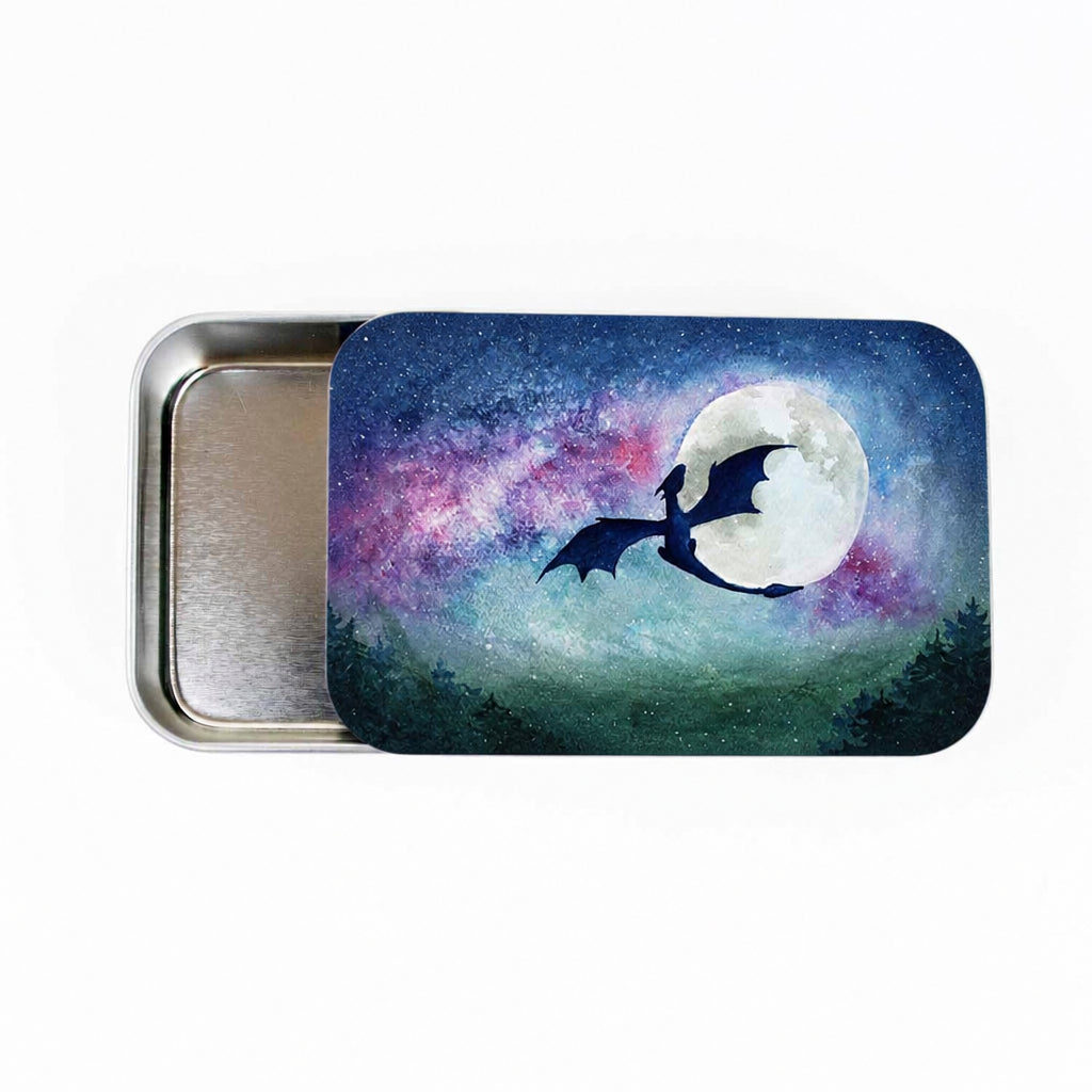 Large slide-style Dragon Moon storage tin with lid partially open, showing watercolor dragon silhouette flying past a full moon against a galaxy night sky with purple nebula and dark forest treeline