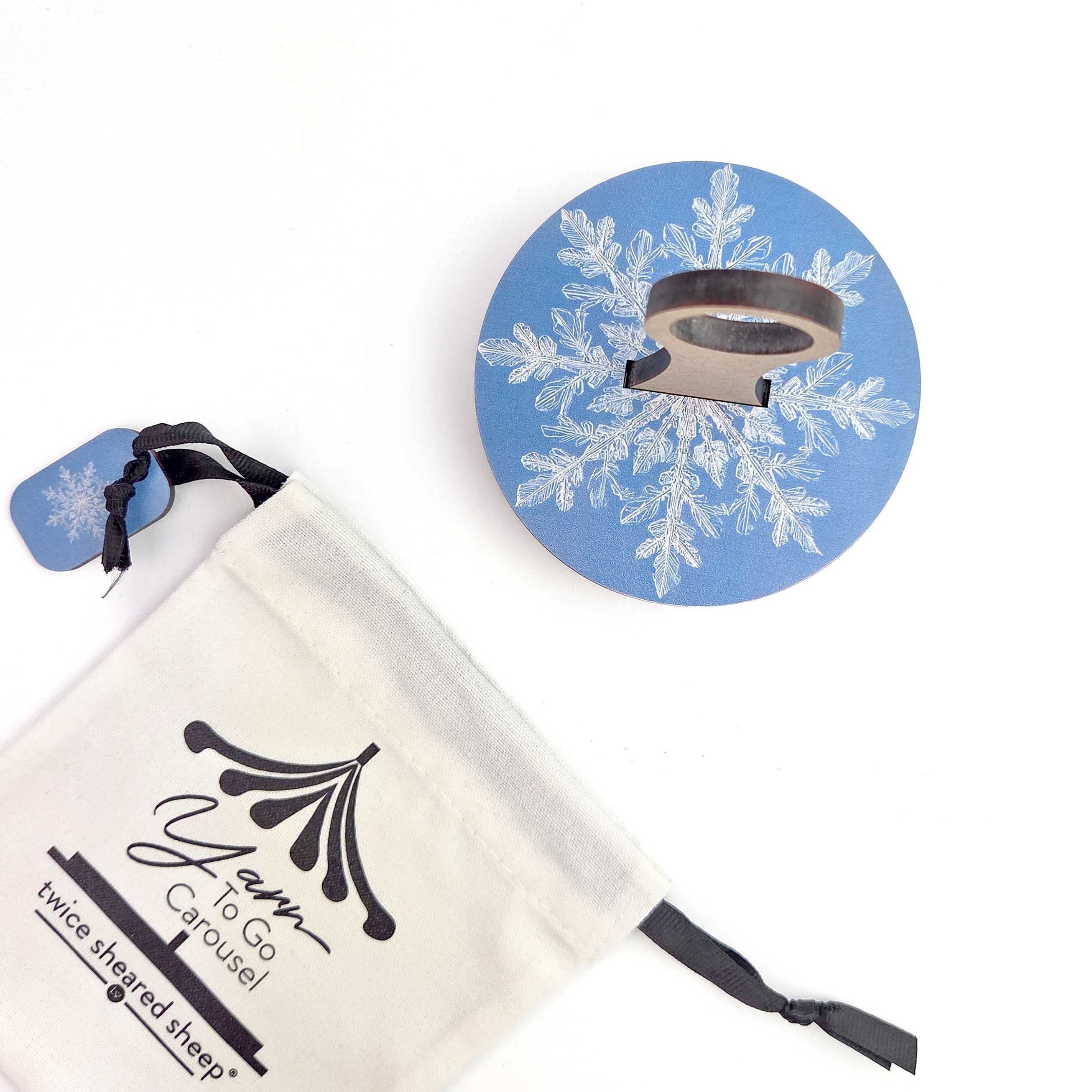 Blue and white snowflake design pin or ornament from the 2026 LYS Exclusive Winter Gift Box with delicate white snowflake pattern on periwinkle blue background