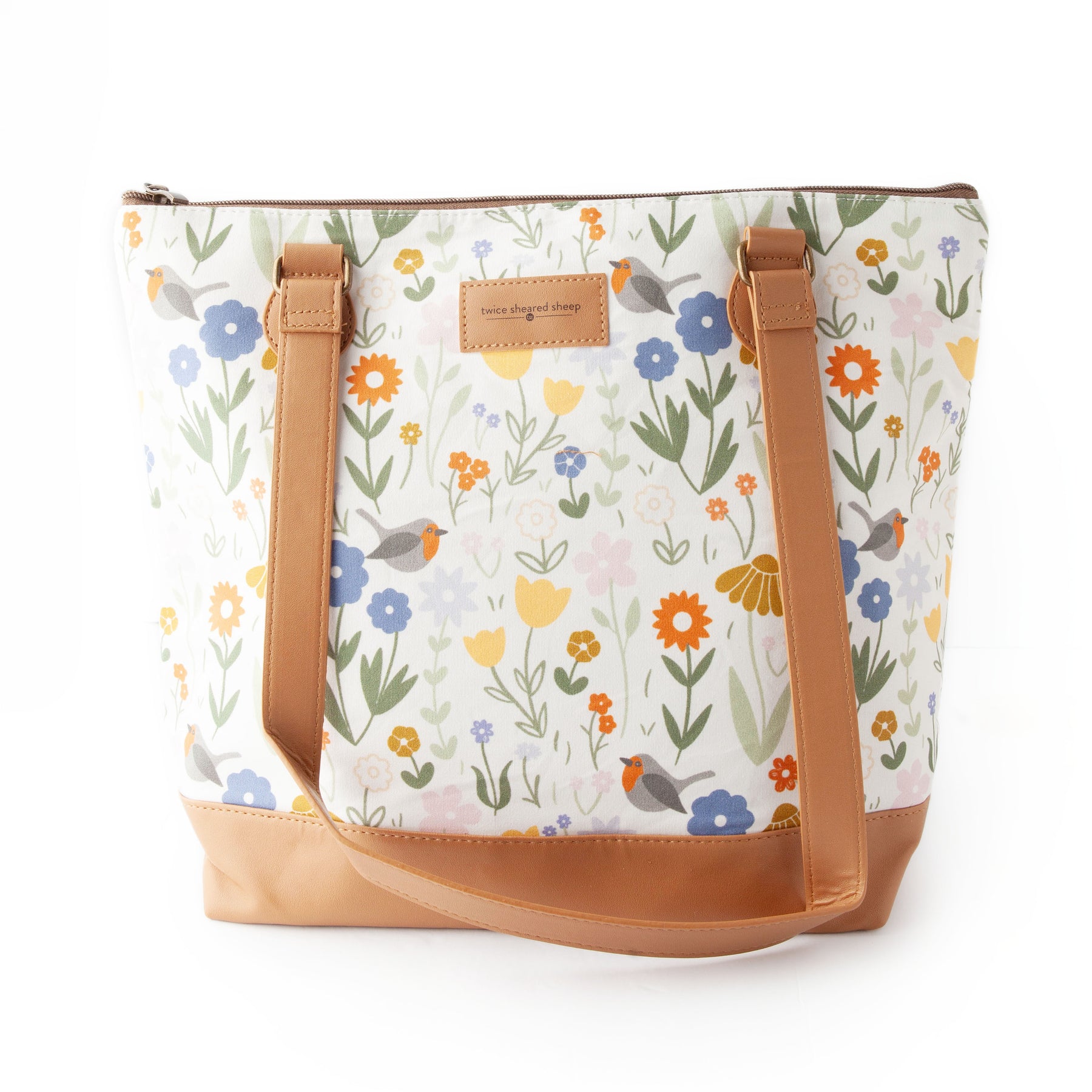 Front view of the Secret Garden tote bag with a white background printed with colorful wildflowers in blue, orange, yellow, and pink with small birds, tan vegan leather bottom and shoulder straps, and a Twice Sheared Sheep leather label
