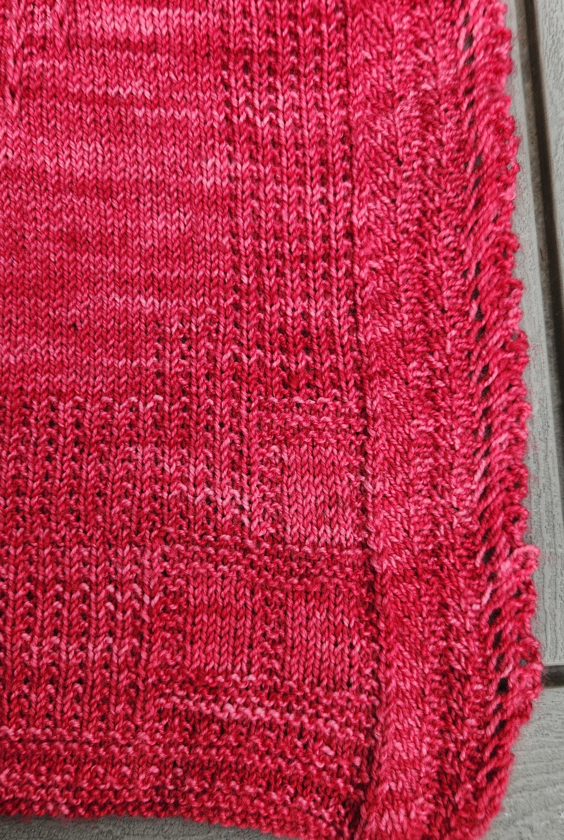 Woman holding the Revenge in Lido Wrap in coral pink up near her face showing the delicate lace openwork stitch pattern