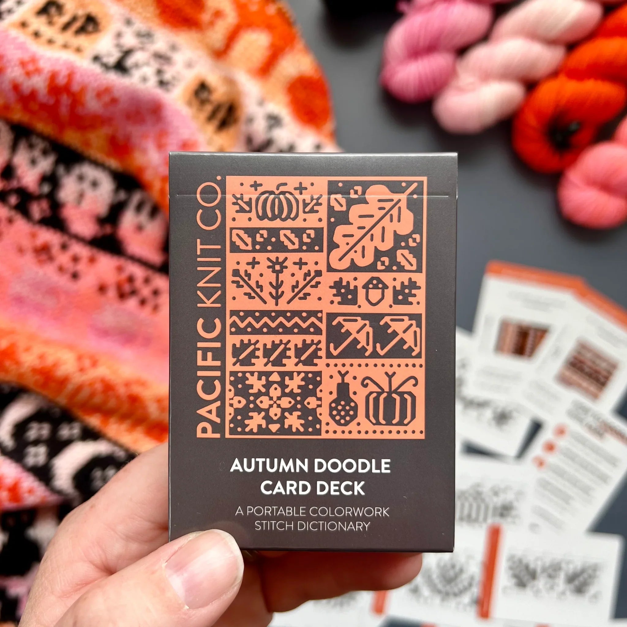 Hand holding the orange and black Autumn Doodle Card Deck by Pacific Knit Co tuckbox