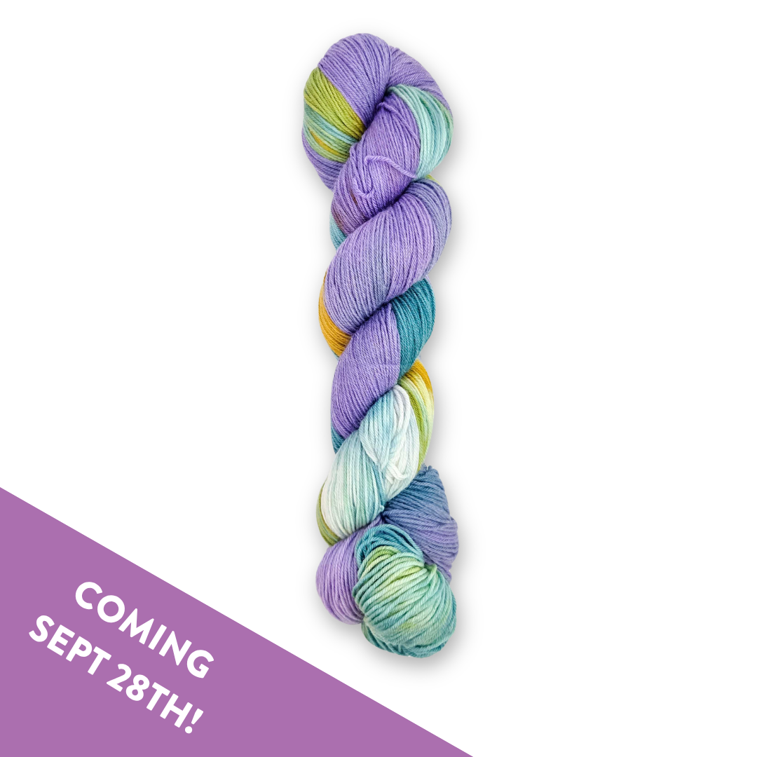 Skein of Molly Klein Design Cove fingering weight sock yarn speckled in lavender, teal, mint and gold, with a Coming Sept 28th banner