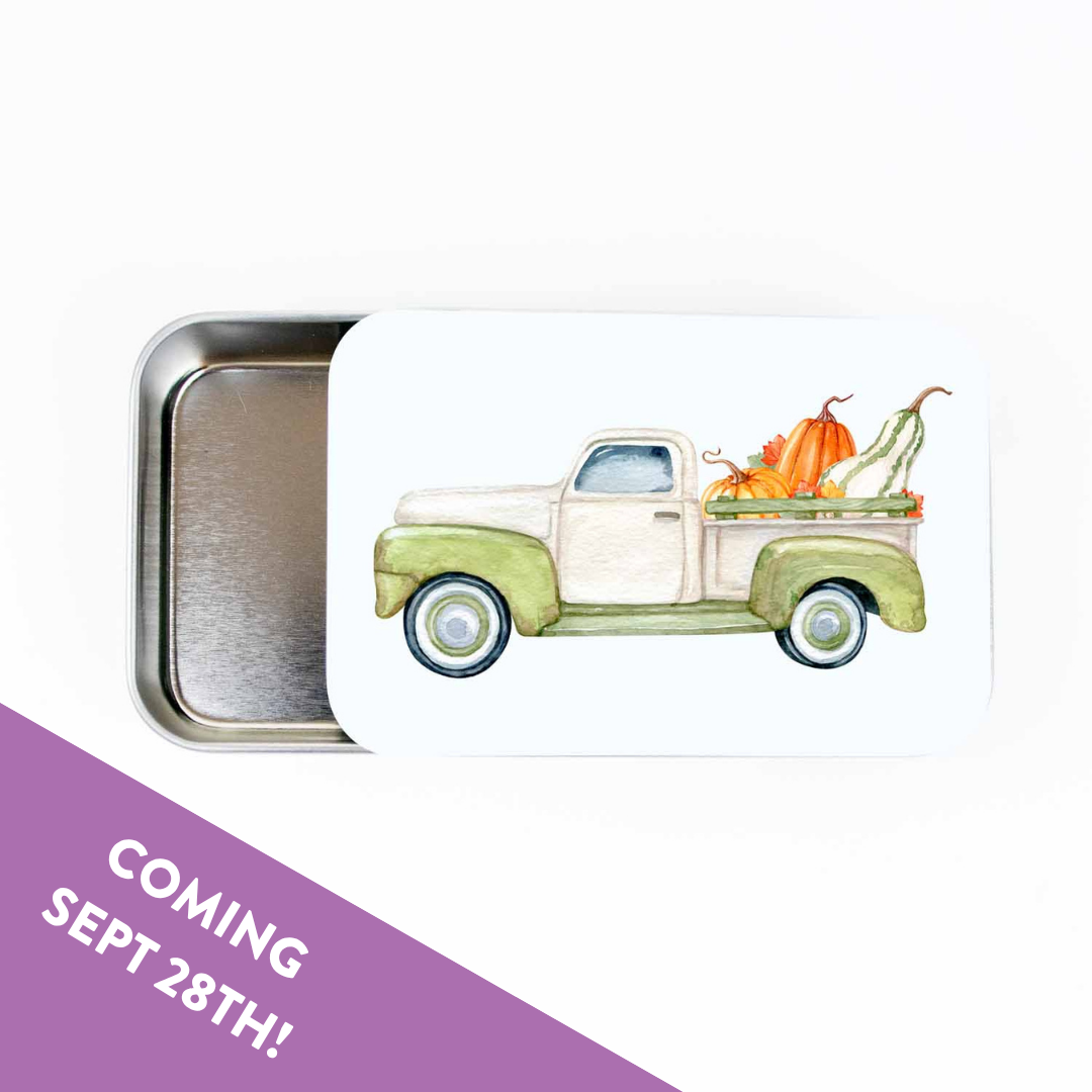 Slide top stitch marker storage tin with a watercolor green pickup truck carrying pumpkins and gourds, with a Coming Sept 28th banner