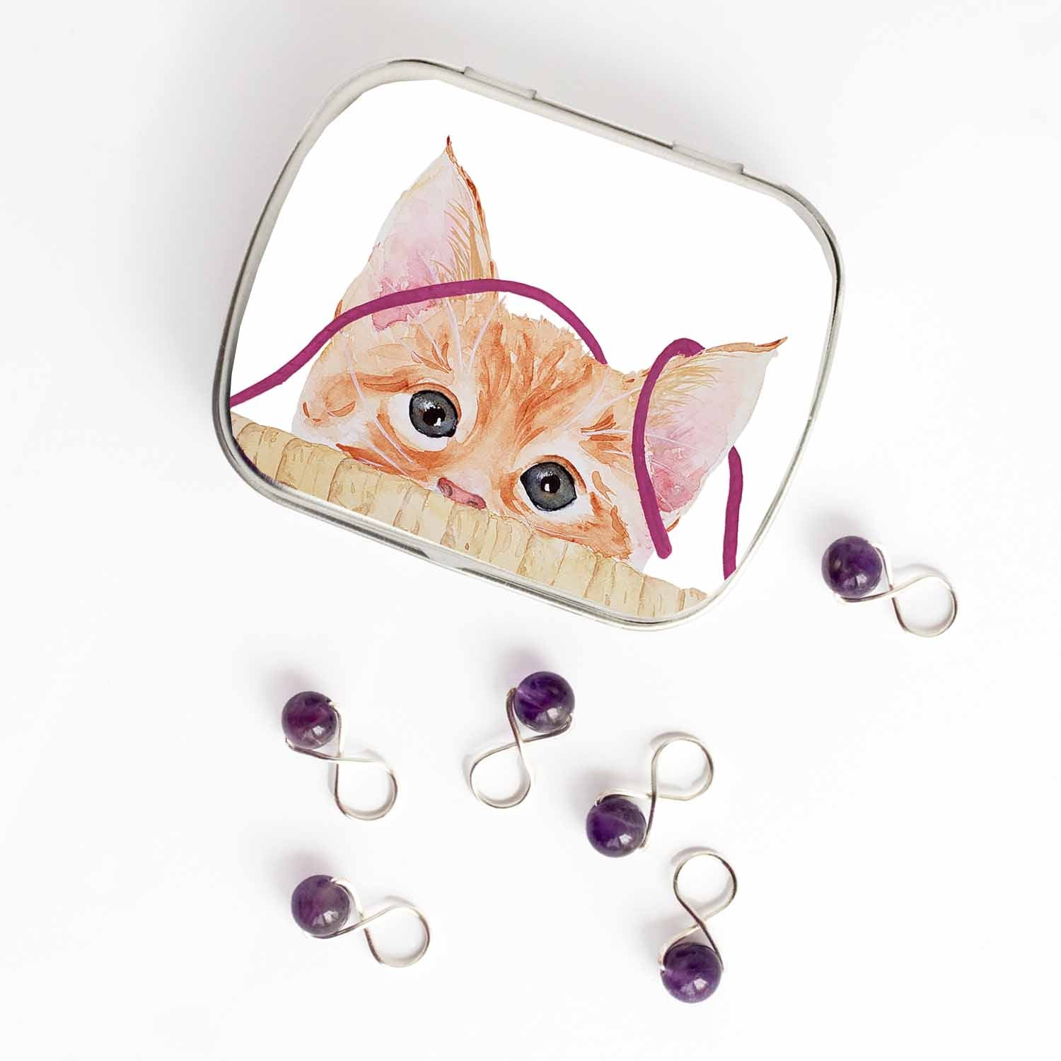 Small hinged Kitten tin with watercolor orange kitten lid, shown beside six purple beaded stitch markers