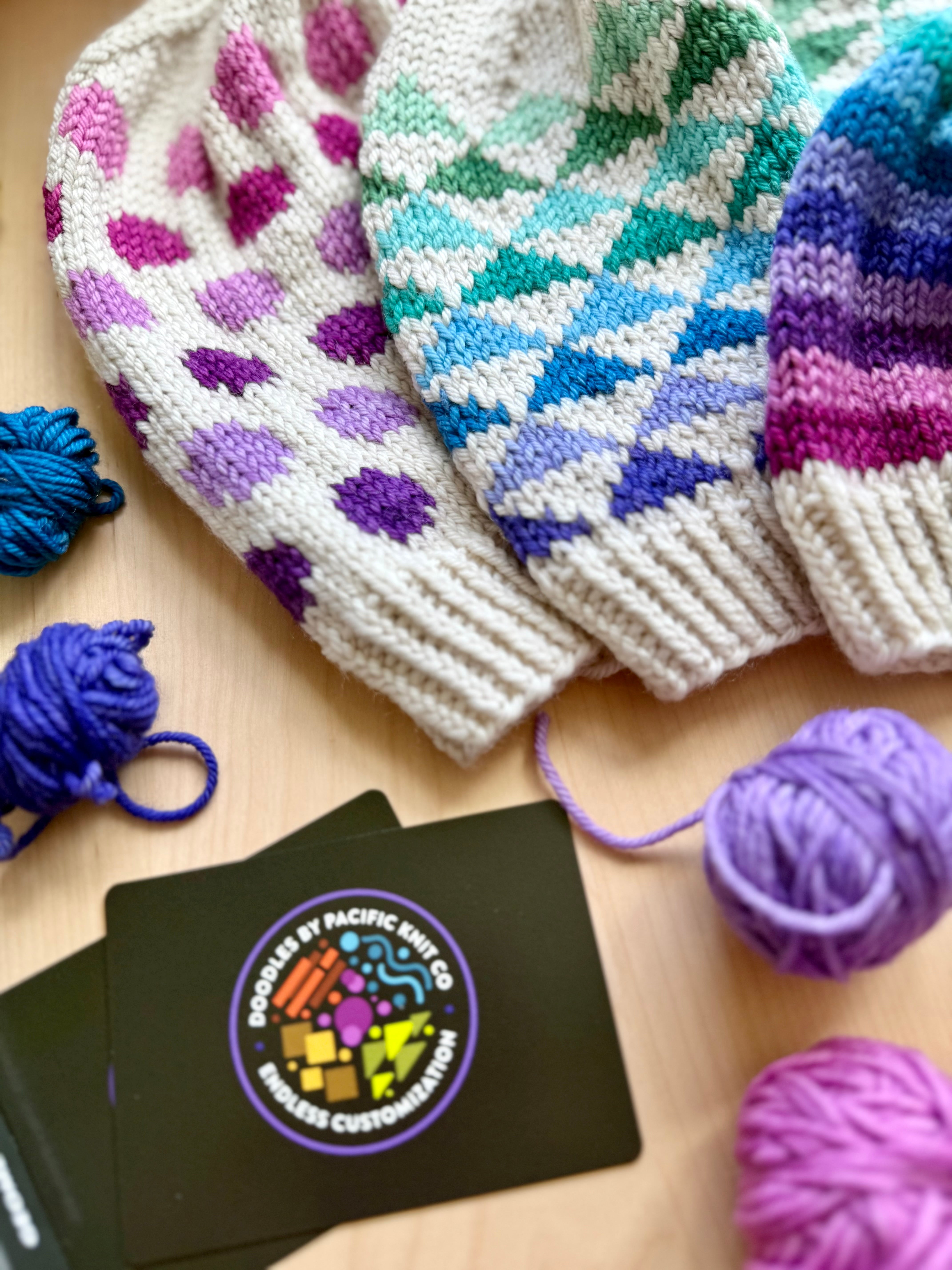 Three Geometric Doodle colorwork hats in purple, teal and pink diamond patterns