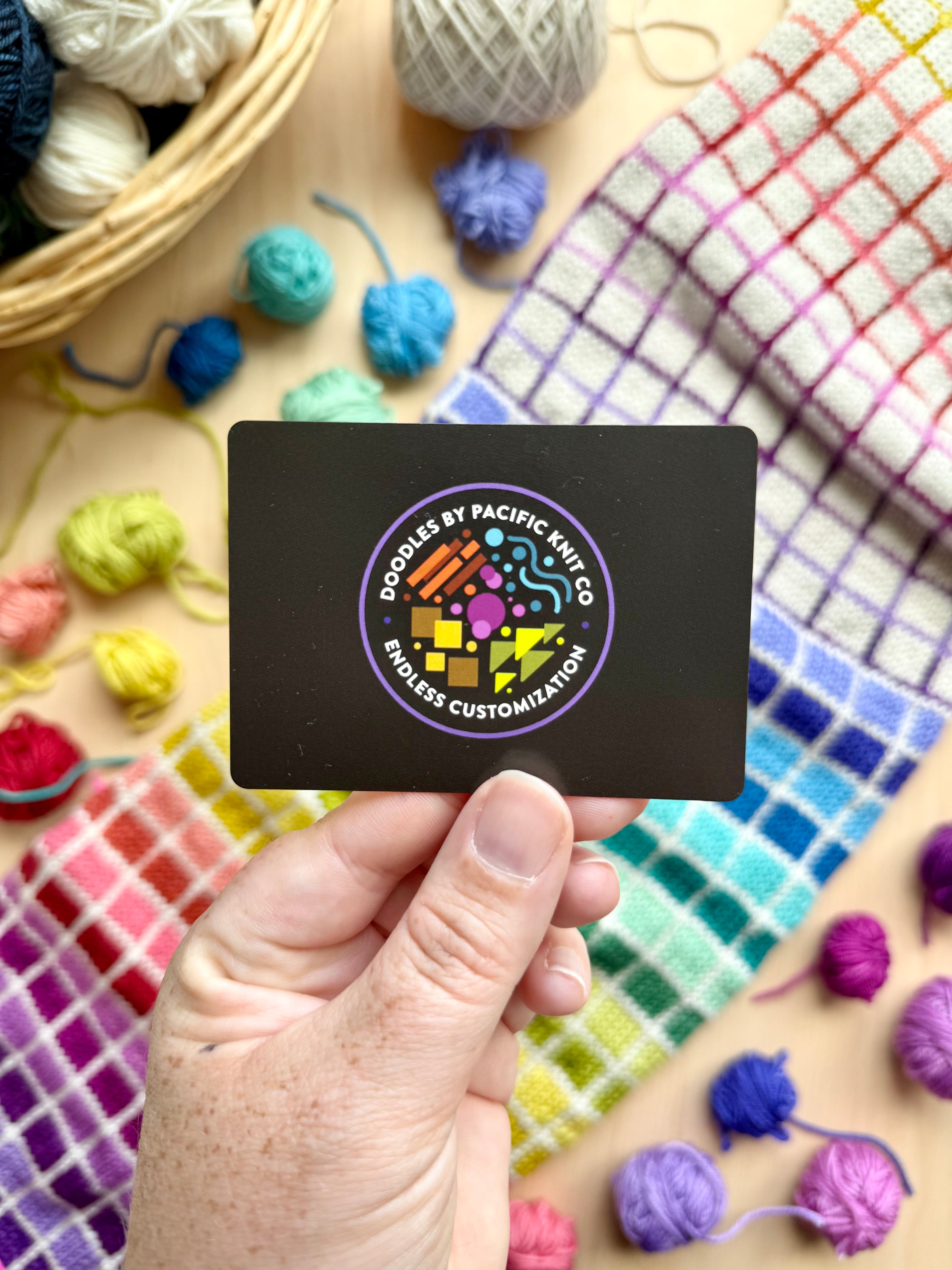 Hand holding the black Pacific Knit Co card back with the Doodles logo