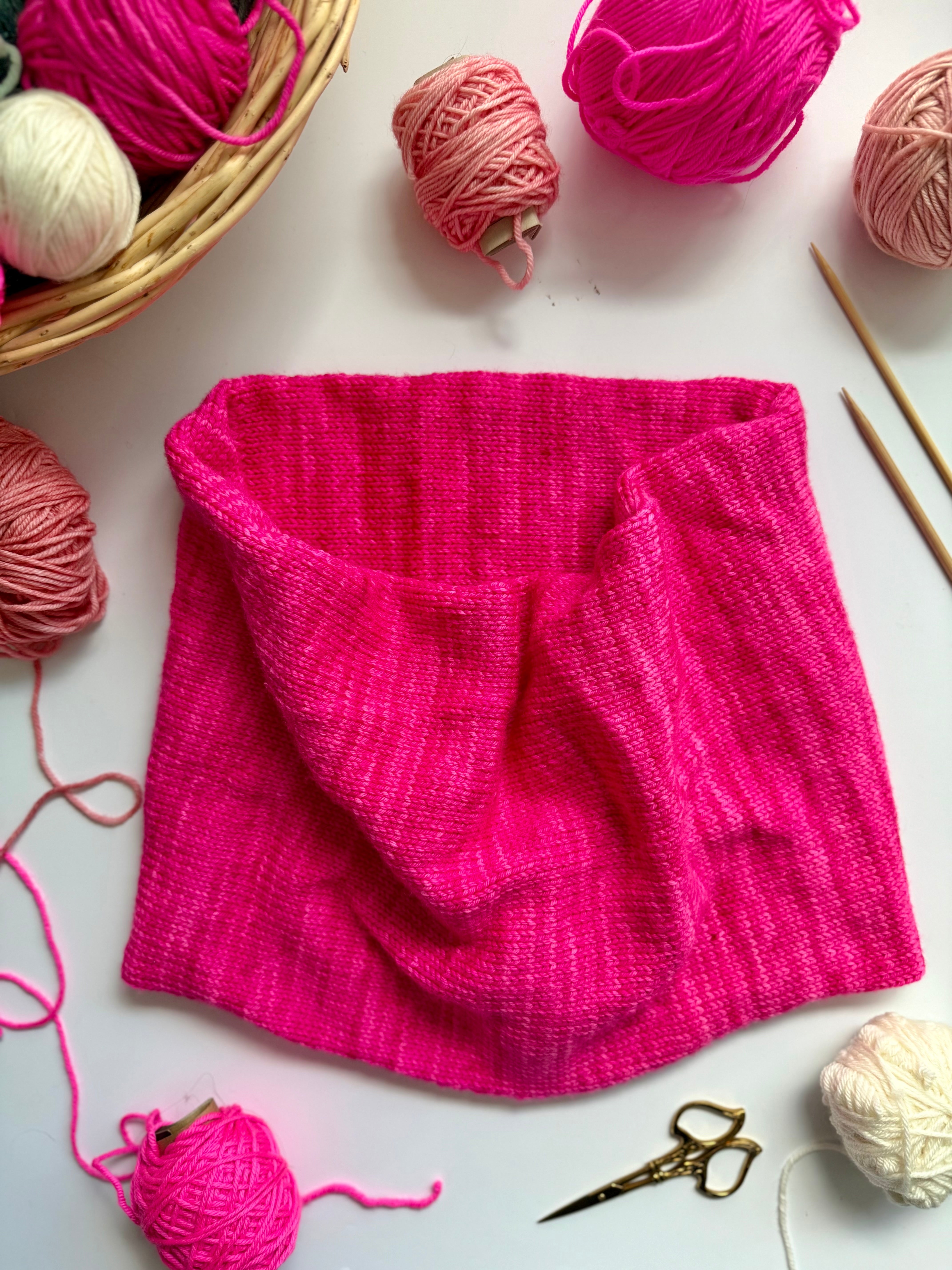 Hot pink Base Doodle Infinity Cowl on a white background with yarn and needles