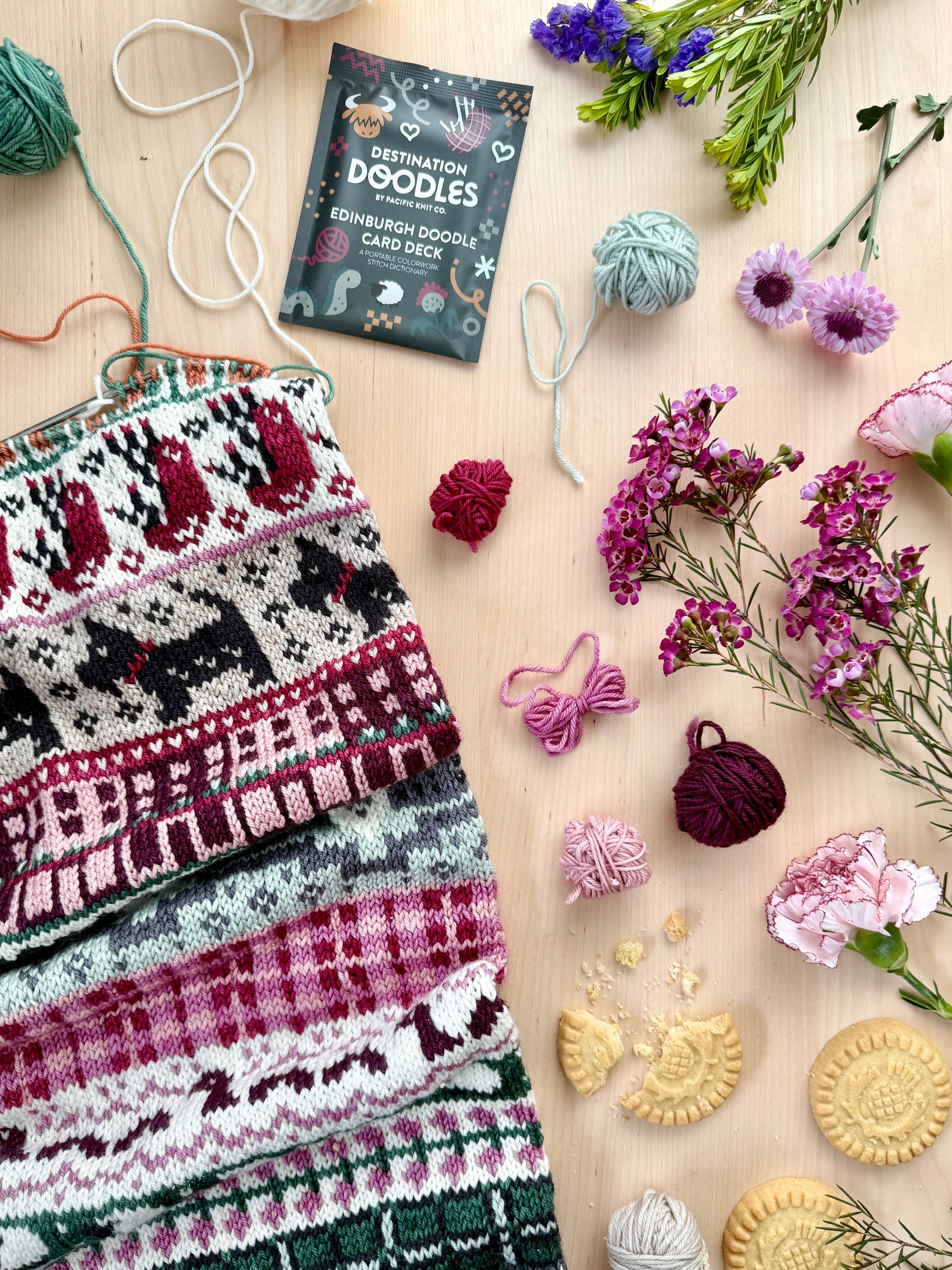 Edinburgh Doodle colorwork knit with Scottish terriers beside the foil pack and flowers