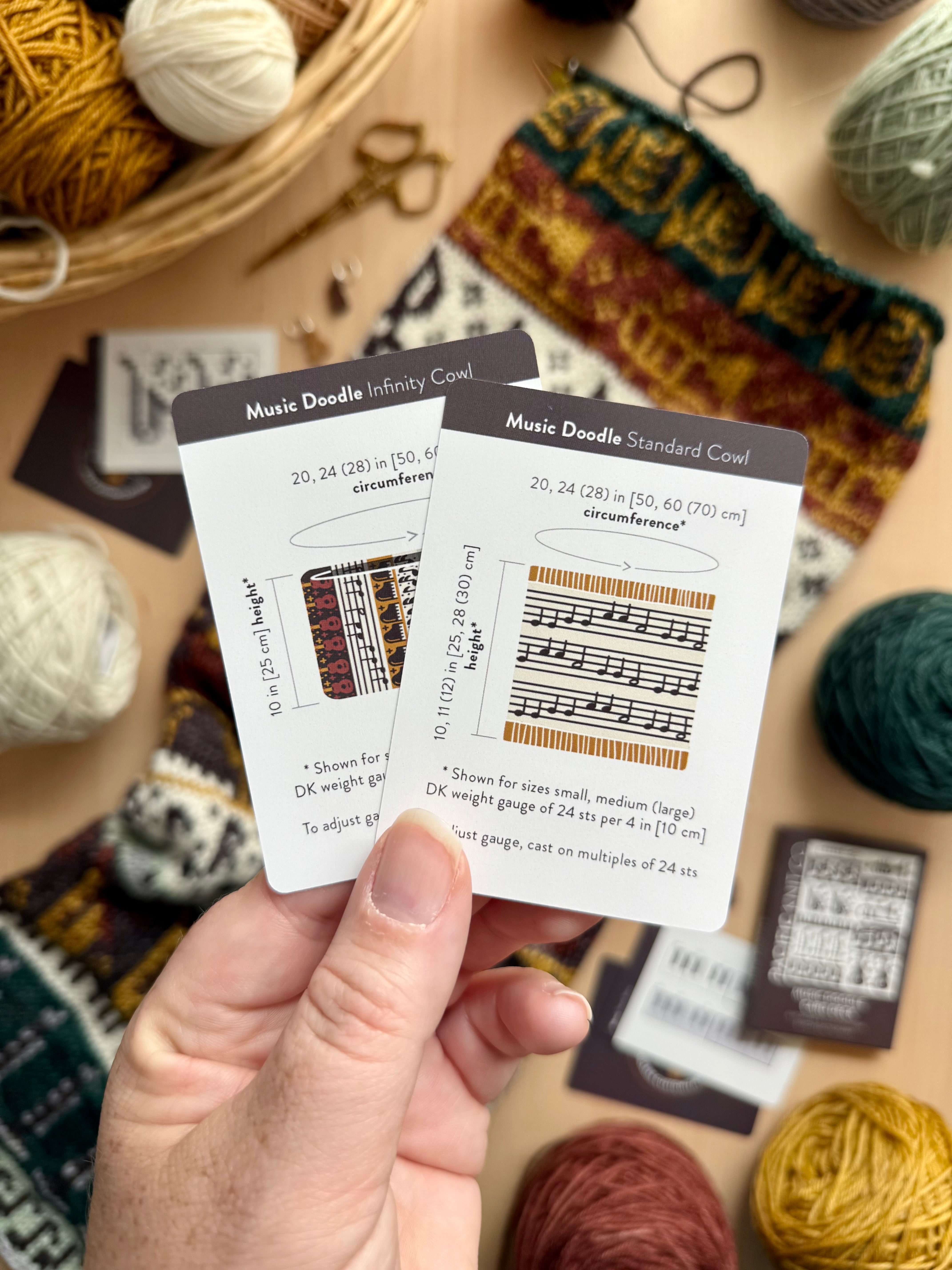 Hand holding the Music Doodle Infinity Cowl and Standard Cowl schematic cards