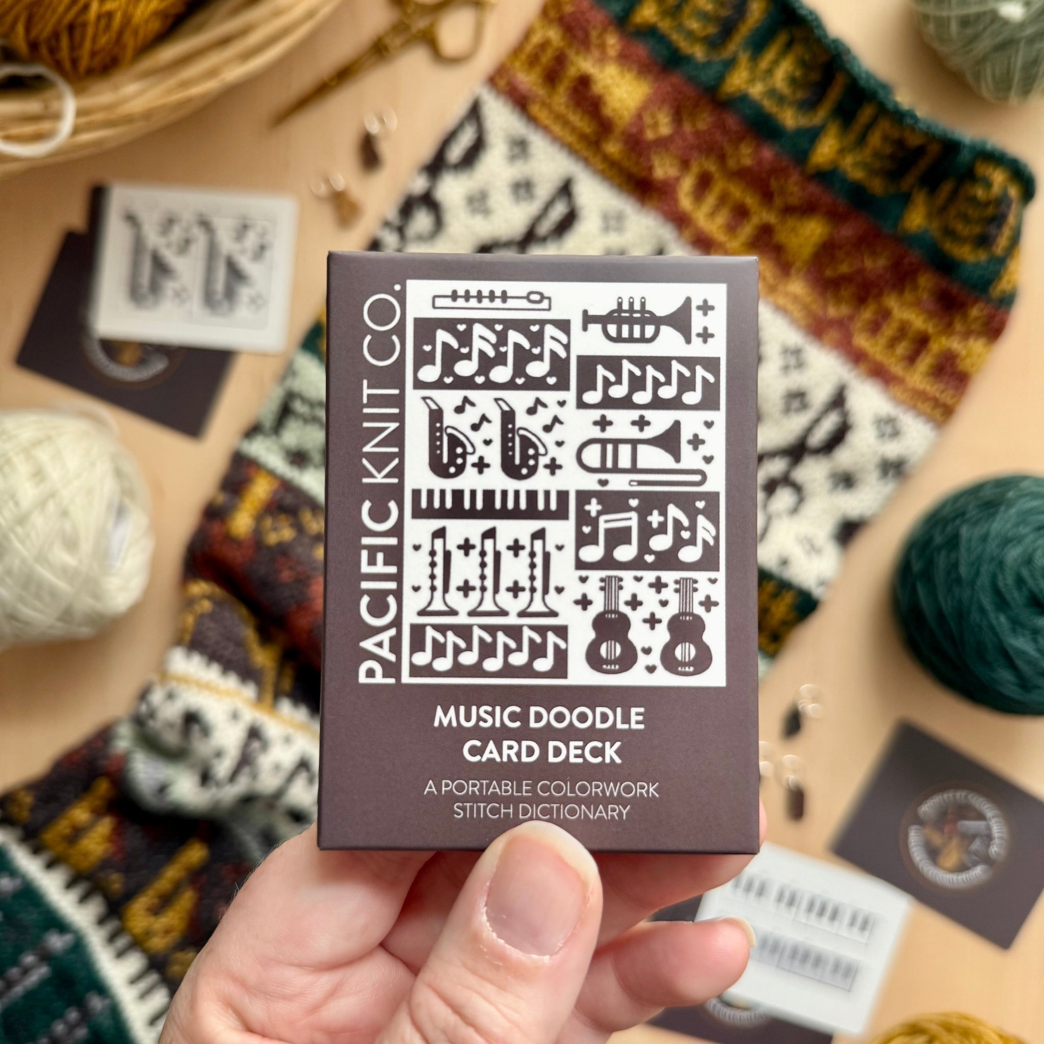 Hand holding the brown Music Doodle Card Deck by Pacific Knit Co tuckbox