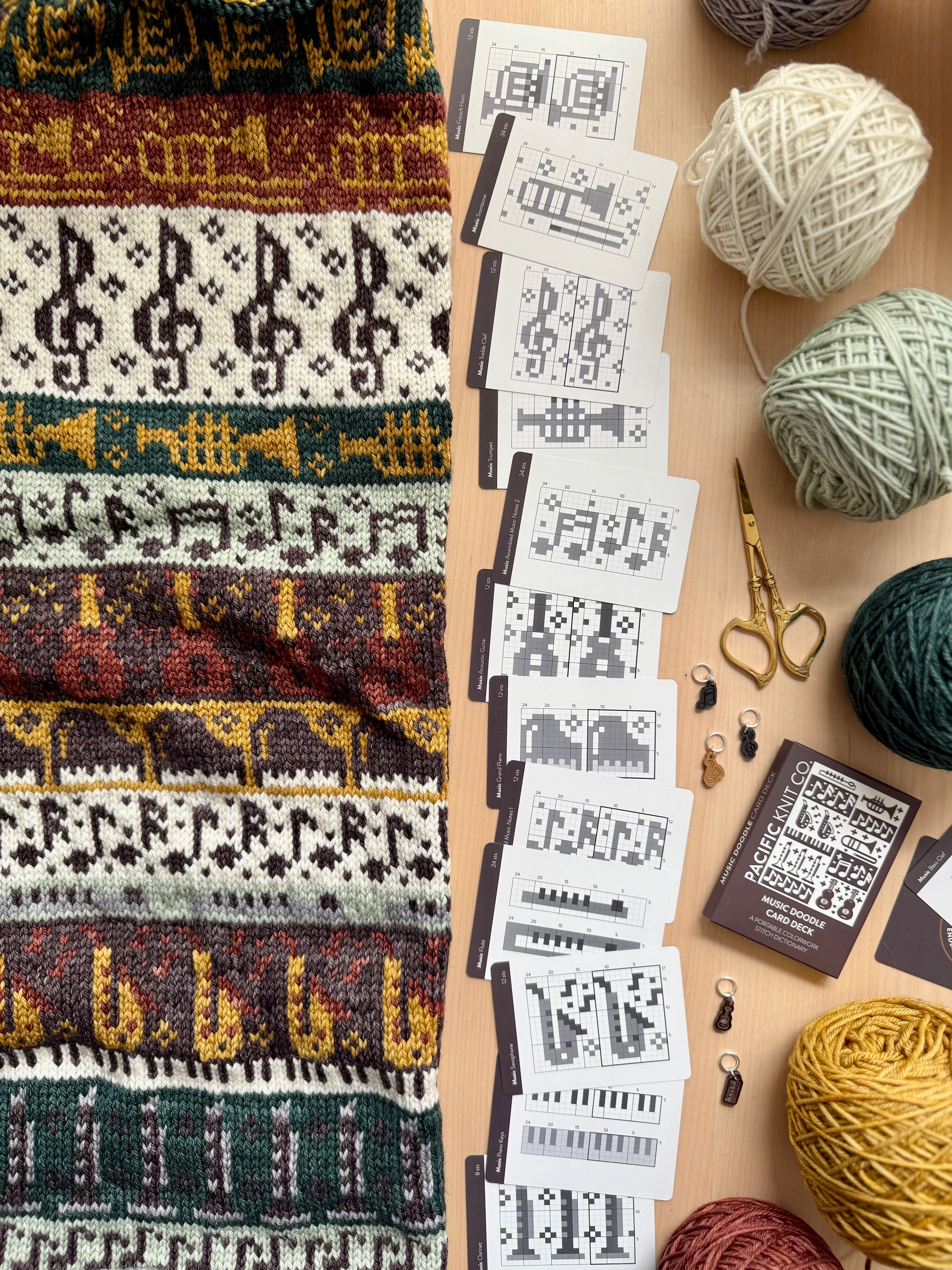 Music Doodle colorwork knit with instrument motifs beside chart cards and yarn