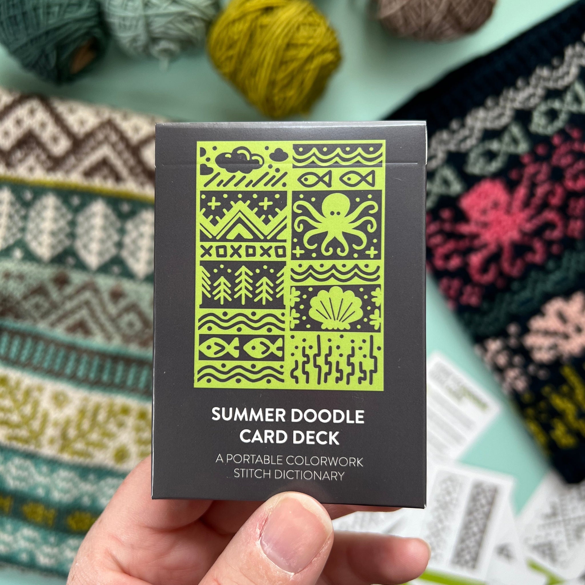 Hand holding the green and black Summer Doodle Card Deck by Pacific Knit Co tuckbox