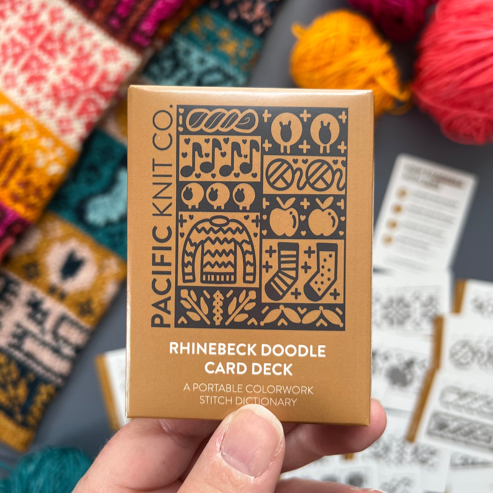 Hand holding the gold Rhinebeck Doodle Card Deck by Pacific Knit Co tuckbox