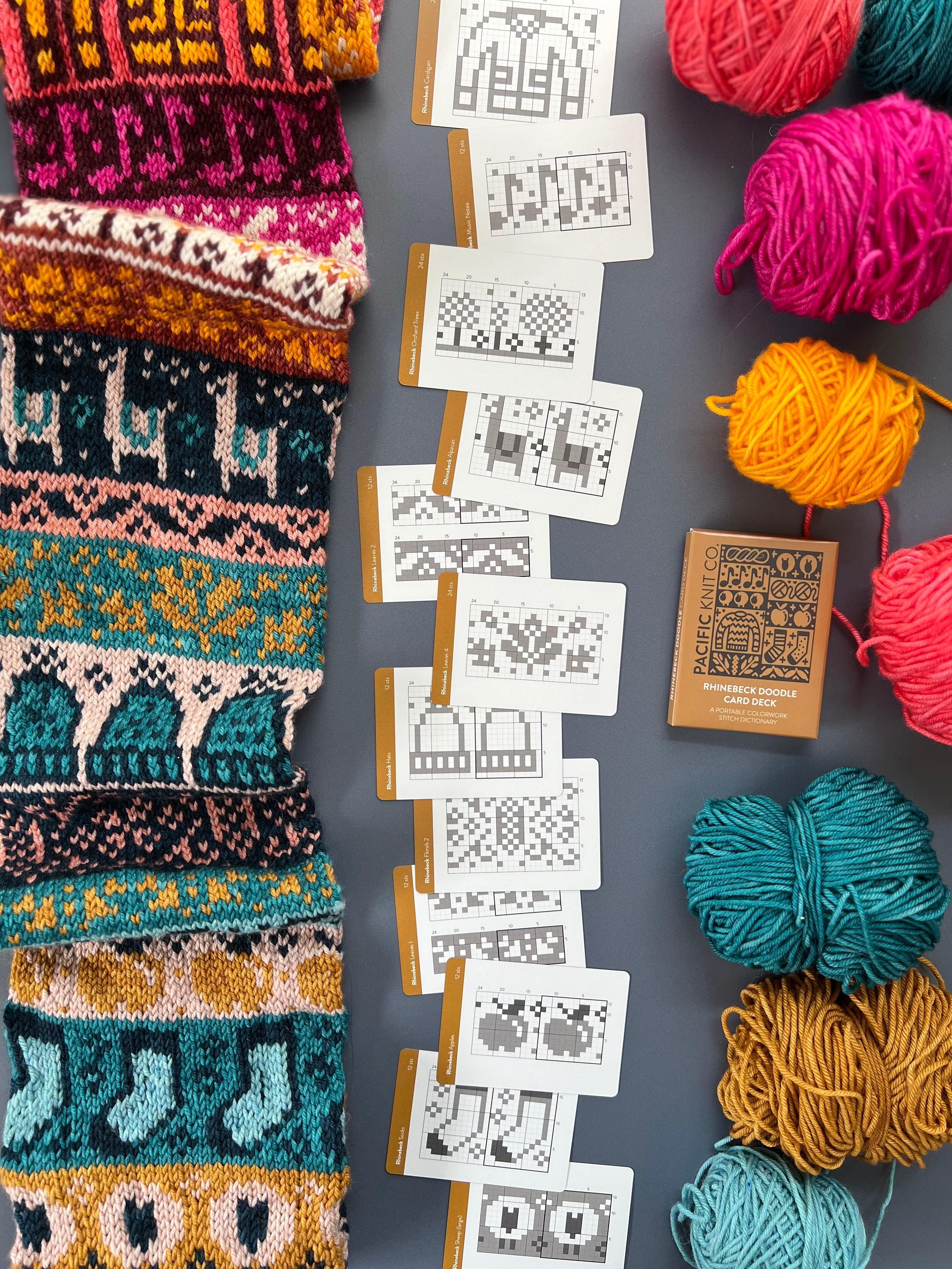 Rhinebeck Doodle chart cards beside a bright colorwork knit and yarn balls