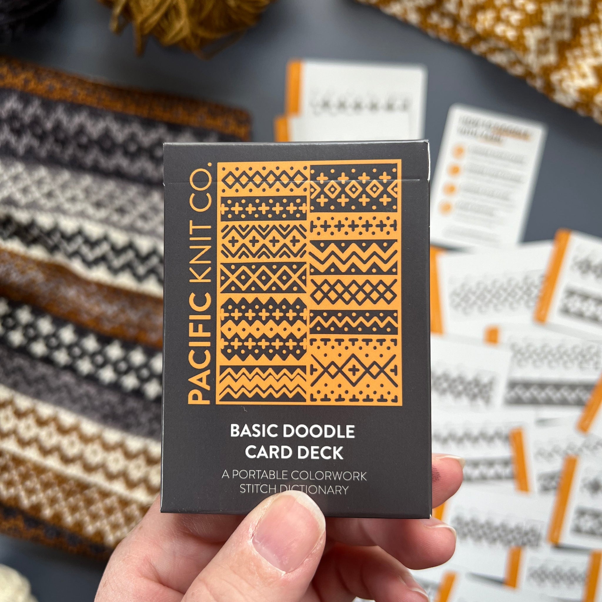 Hand holding the orange and black Basic Doodle Card Deck by Pacific Knit Co tuckbox