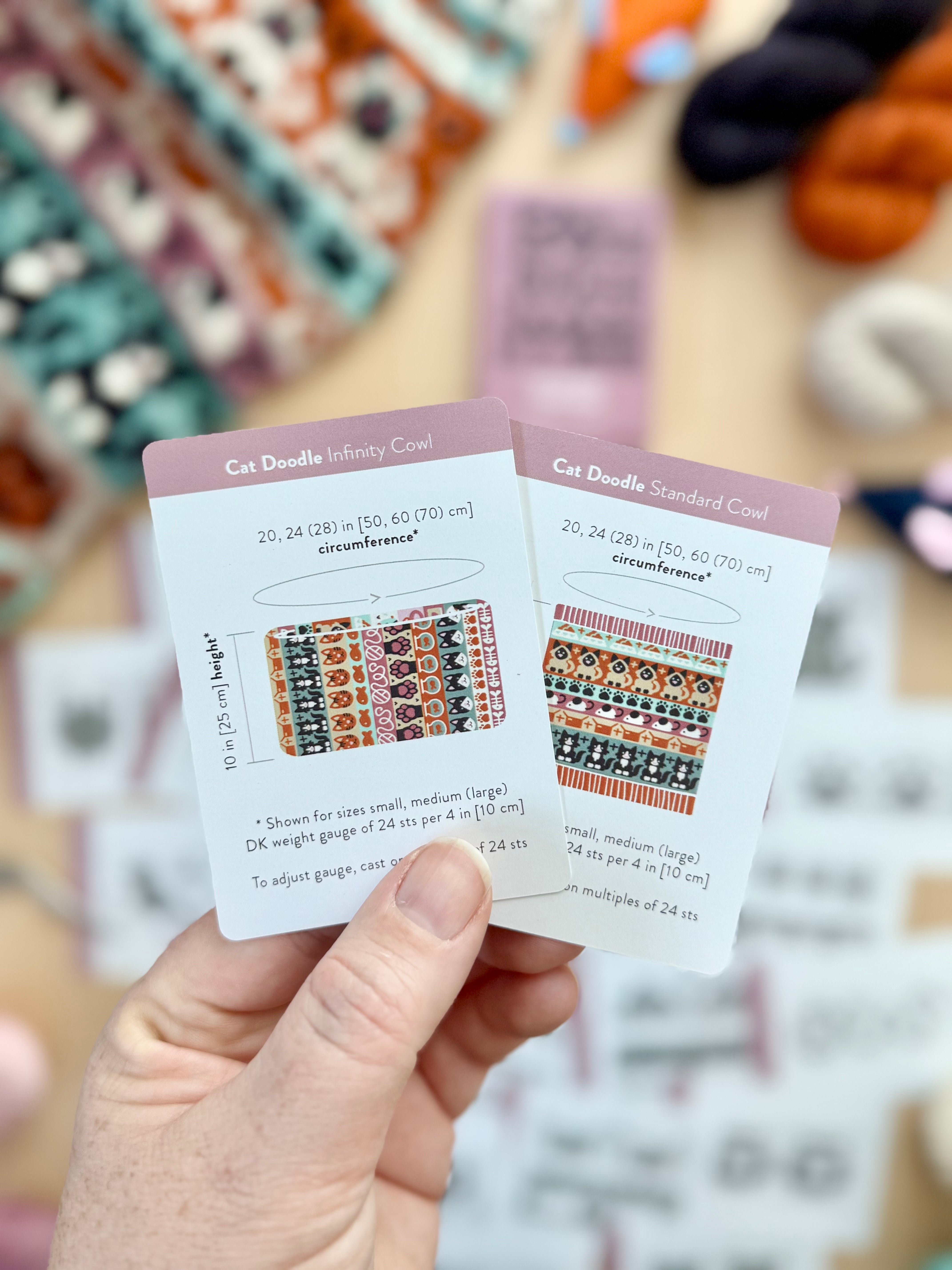 Hand holding the Cat Doodle Infinity Cowl and Standard Cowl schematic cards