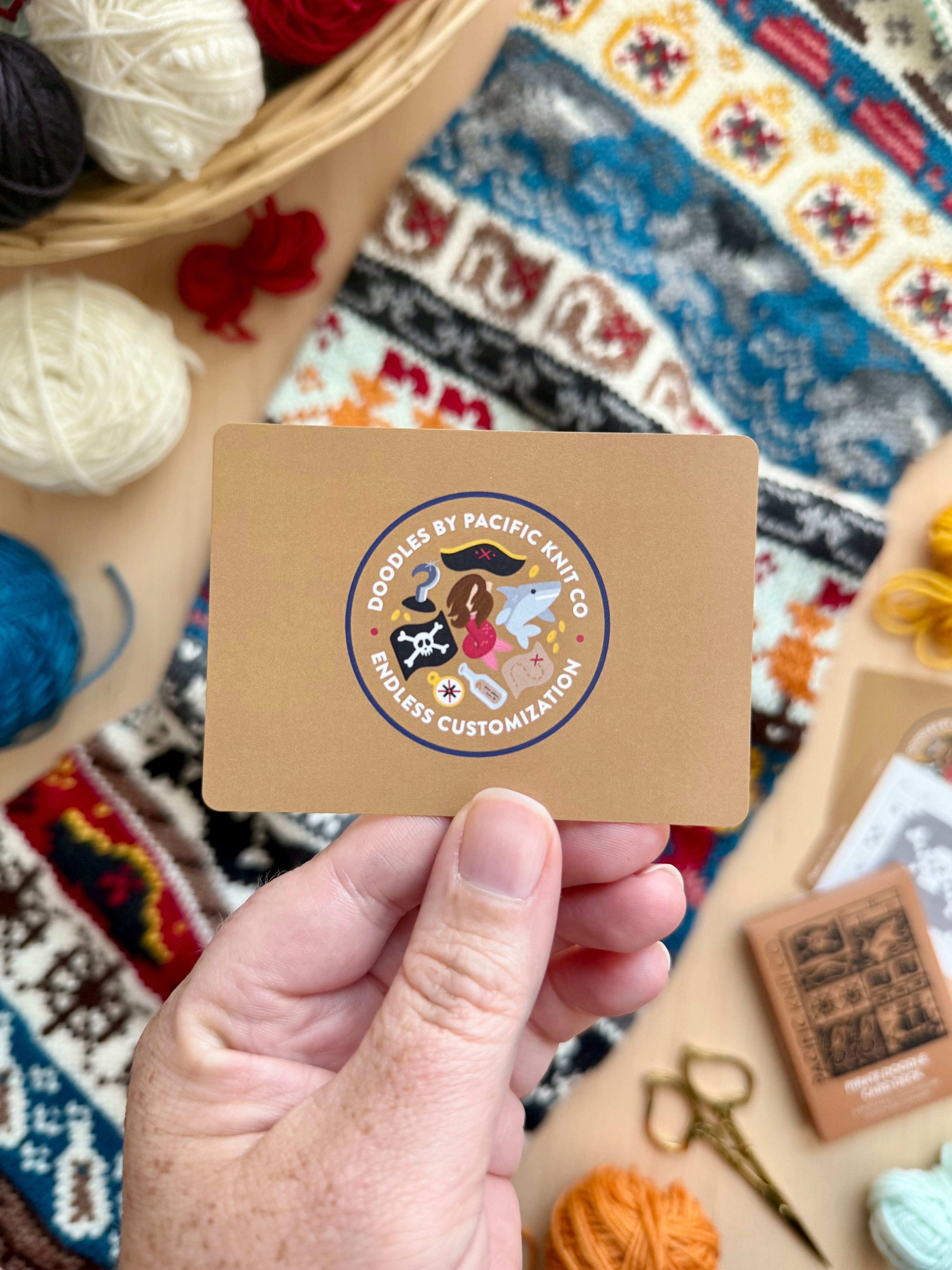 Hand holding the tan Pacific Knit Co card back with the Doodles logo