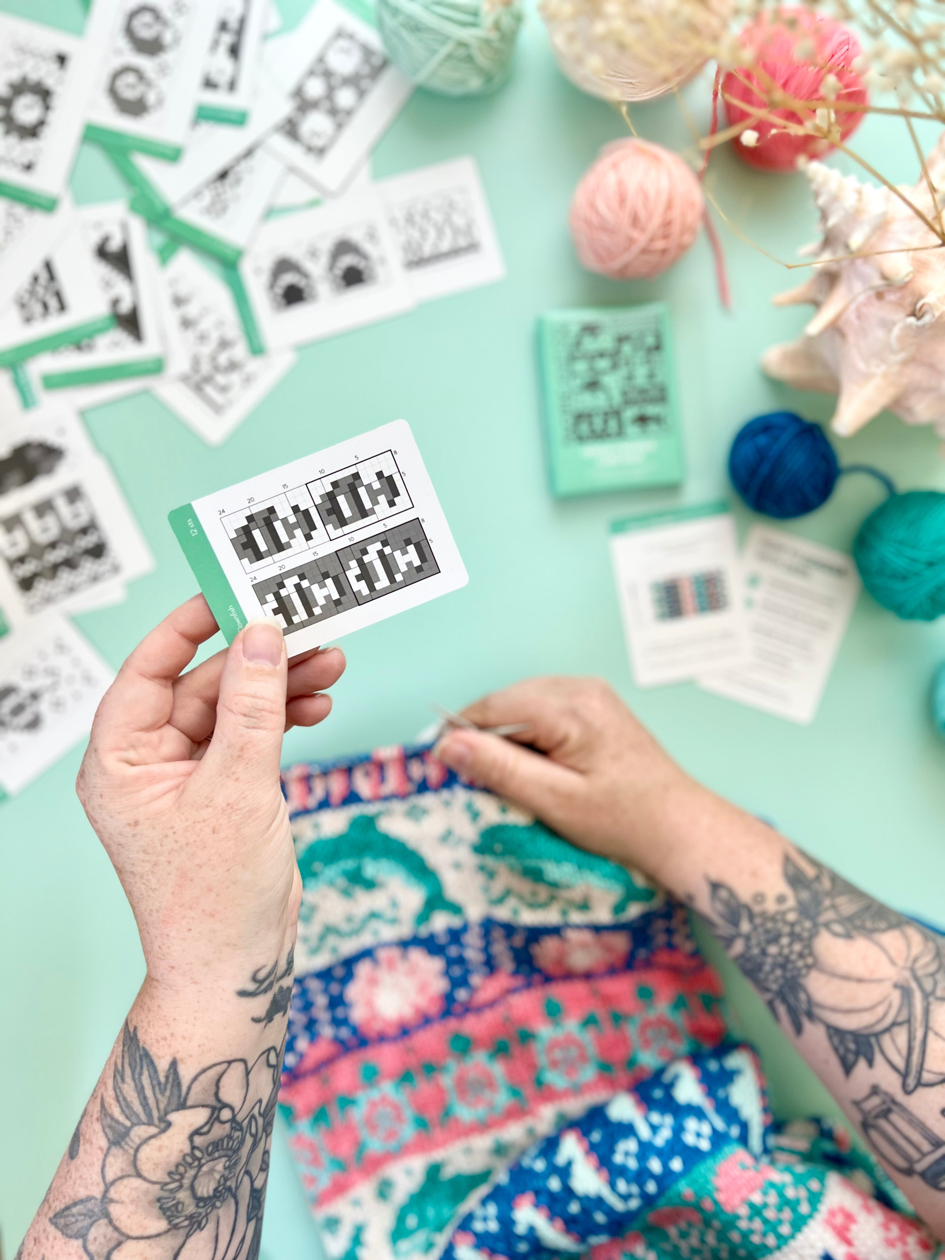 Hand picking up an Ocean 2 Doodle chart card above a sea life colorwork knit