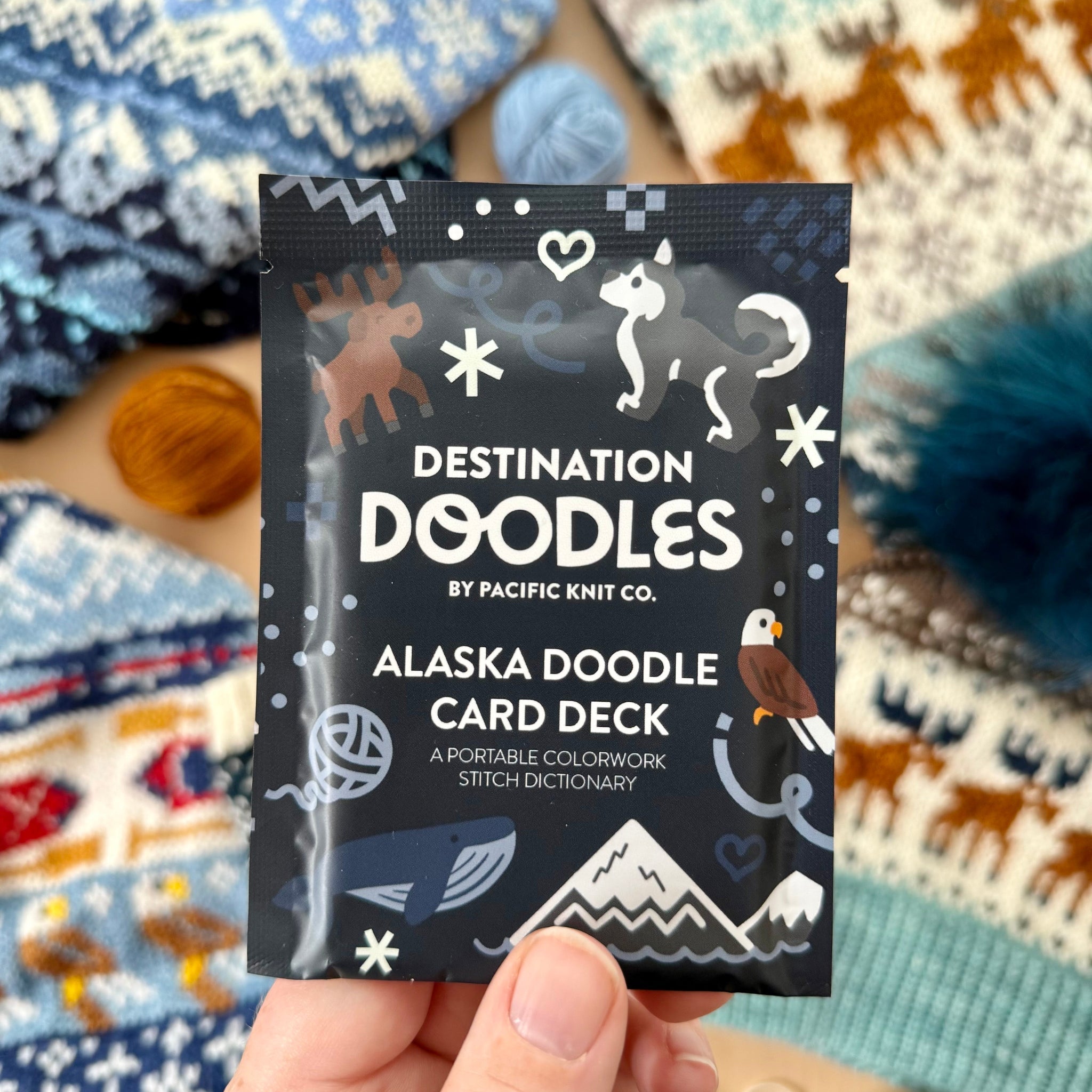 Hand holding the navy Alaska Destination Doodle Card Deck foil pack by Pacific Knit Co