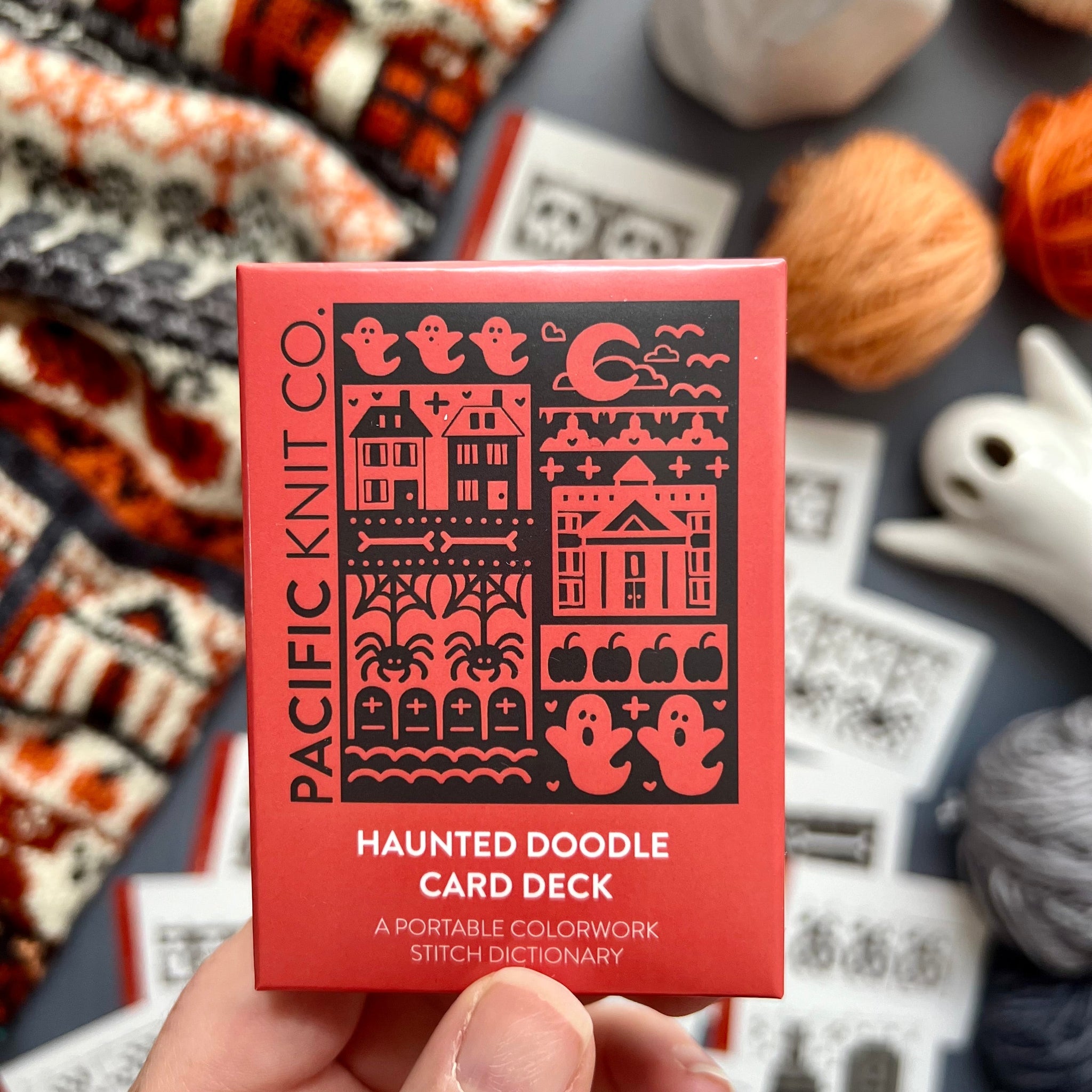 Hand holding the red Haunted Doodle Card Deck by Pacific Knit Co tuckbox
