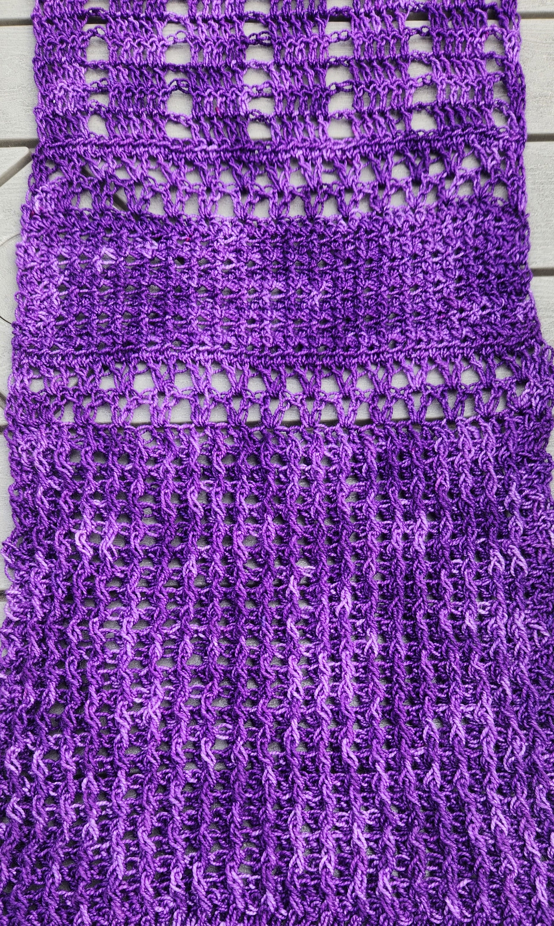 Extreme close-up of the Galliano Revenge Wrap stitch detail showing the front and back post double crochet texture creating geometric checked boxes alongside open mesh sections in rich variegated purple yarn