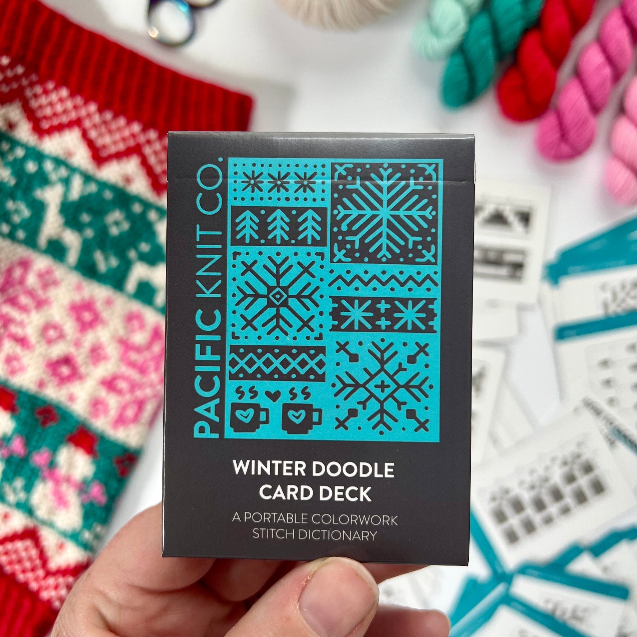 Hand holding the teal and black Winter Doodle Card Deck by Pacific Knit Co tuckbox
